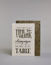 Karte in Englisch mit der Aufschrift „Time to drink champagne and dance on the table“ in dekorativer Handlettering-Schrift auf hellem Hintergrund. Die Wörter sind in Schwarz gestaltet, teils mit goldfarbenen und glitzernden Details hervorgehoben. Das "TIME TO DRINK" und "TABLE" ist in kreativer gerader Kalligrafieaufschrift gestaltet, das "Champagne" in geschwungener und das "AND DANCE ON THE" in dünner gerader Schrift. Dazu ein grün-goldenes handgeschöpftes Kuvert. #2