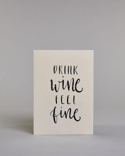 Karte in Englisch mit der Aufschrift „Drink wine feel fine“ in schwarzer Handlettering-Schrift, teils mit kleinen goldfarbenen Akzenten auf vier Zeilen mit jeweils immer einem Wort aufgeteilt und auf hellem Hintergrund. Dazu ein grün-goldenes handgeschöpftes Kuvert. #1