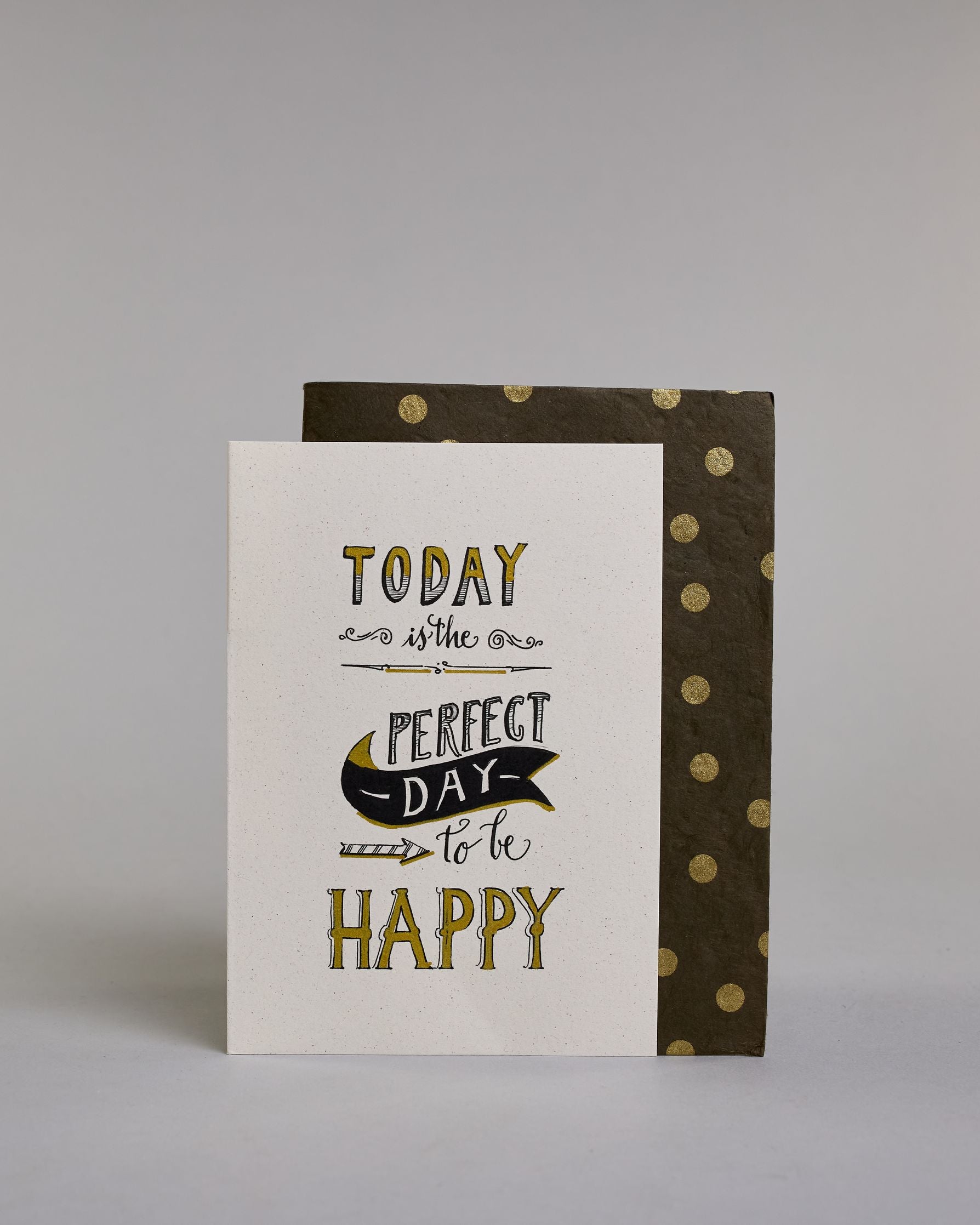 Karte in Englisch mit der Aufschrift „Today is the perfect day to be happy“ in dekorativer Handlettering-Schrift. Die Wörter „TODAY“, „PERFECT DAY“ und „HAPPY“ sind mit goldfarbenen Akzenten hervorgehoben. Ein schwarzes Bannerl ergänzet das Design, in diesem befindet sich das Wort "DAY", darunter ist ein nach rechts, zu den Wörtern "to be" zeigender Pfeil auf hellem Hintergrund. Dazu ein grün-goldenes handgeschöpftes Kuvert. #2