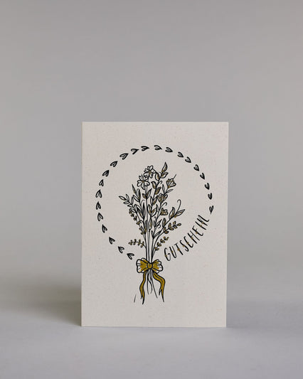 Gutschein-Karte mit einem gezeichneten Blumenstrauß aus filigranen Blüten und Zweigen, zusammengebunden mit einer goldfarbenen Schleife. Um den Strauß verläuft ein Herzkranz. Rechts neben dem Strauß steht das Wort „Gutschein“ in schwarzer Schrift in den Kranz eingearbeitet auf hellem Hintergrund. Dazu ein grün-goldenes handgeschöpftes Kuvert. #1