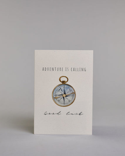 Karte mit der Aufschrift „Adventure is calling Good luck“ in schwarzer Kalligrafieaufschrift. In der Mitte ist eine detailreich gezeichnete Kompass-Illustration mit goldenem Rand und goldener Nadel abgebildet, die Innenseite des Kompasses ist hellblau und die Karte selbst bildet einen hellen Hintergrund. Dazu ein grün-goldenes handgeschöpftes Kuvert. #1