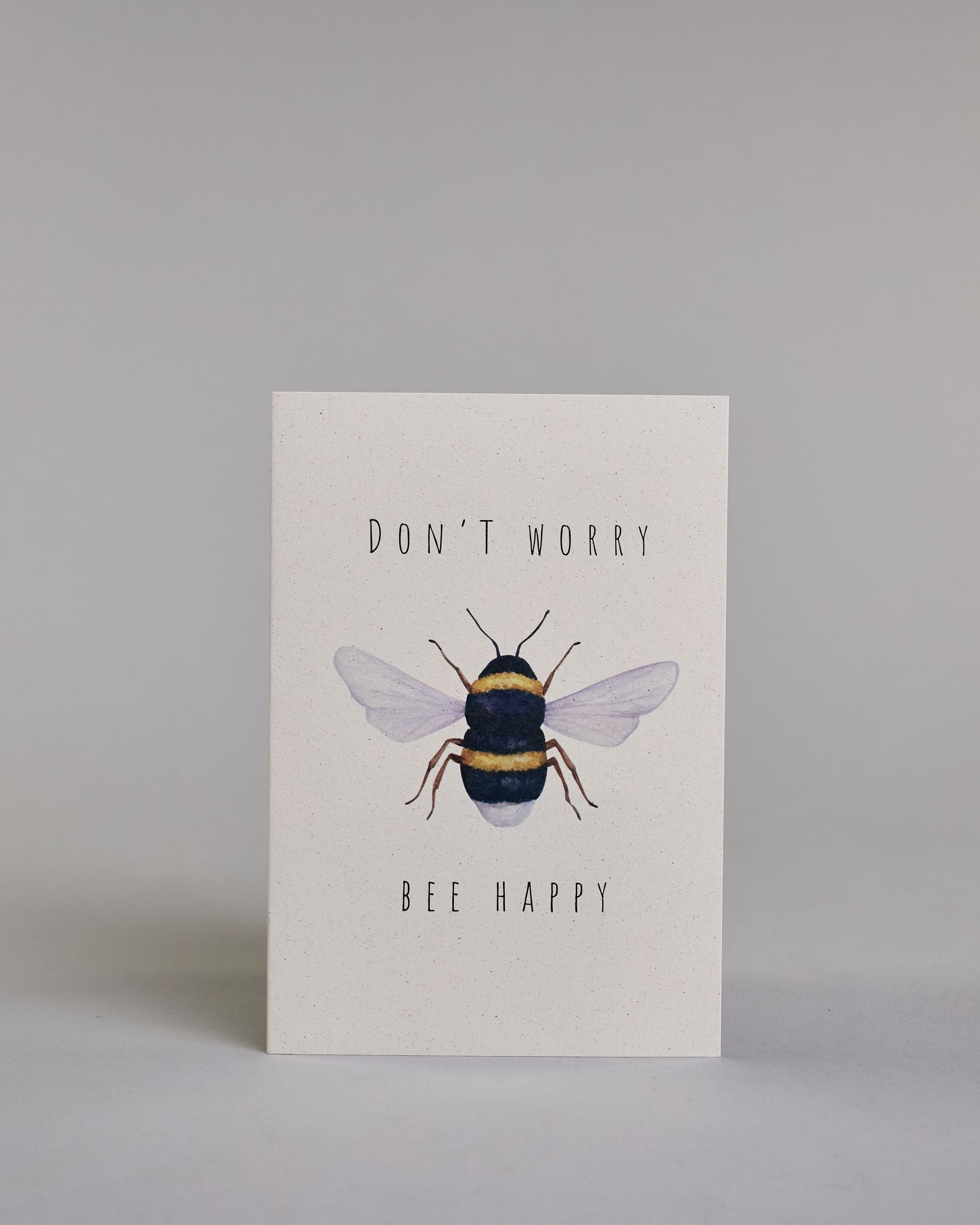 Karte auf Englisch mit der Aufschrift „Don’t worry Bee happy“ in schwarzer Schrift auf hellem Hintergrund. In der Mitte ist eine detailreich gezeichnete Biene mit gelb-schwarzem Körper und durchscheinenden Flügeln abgebildet. Dazu ein weißes handgeschöpftes Kuvert. #1