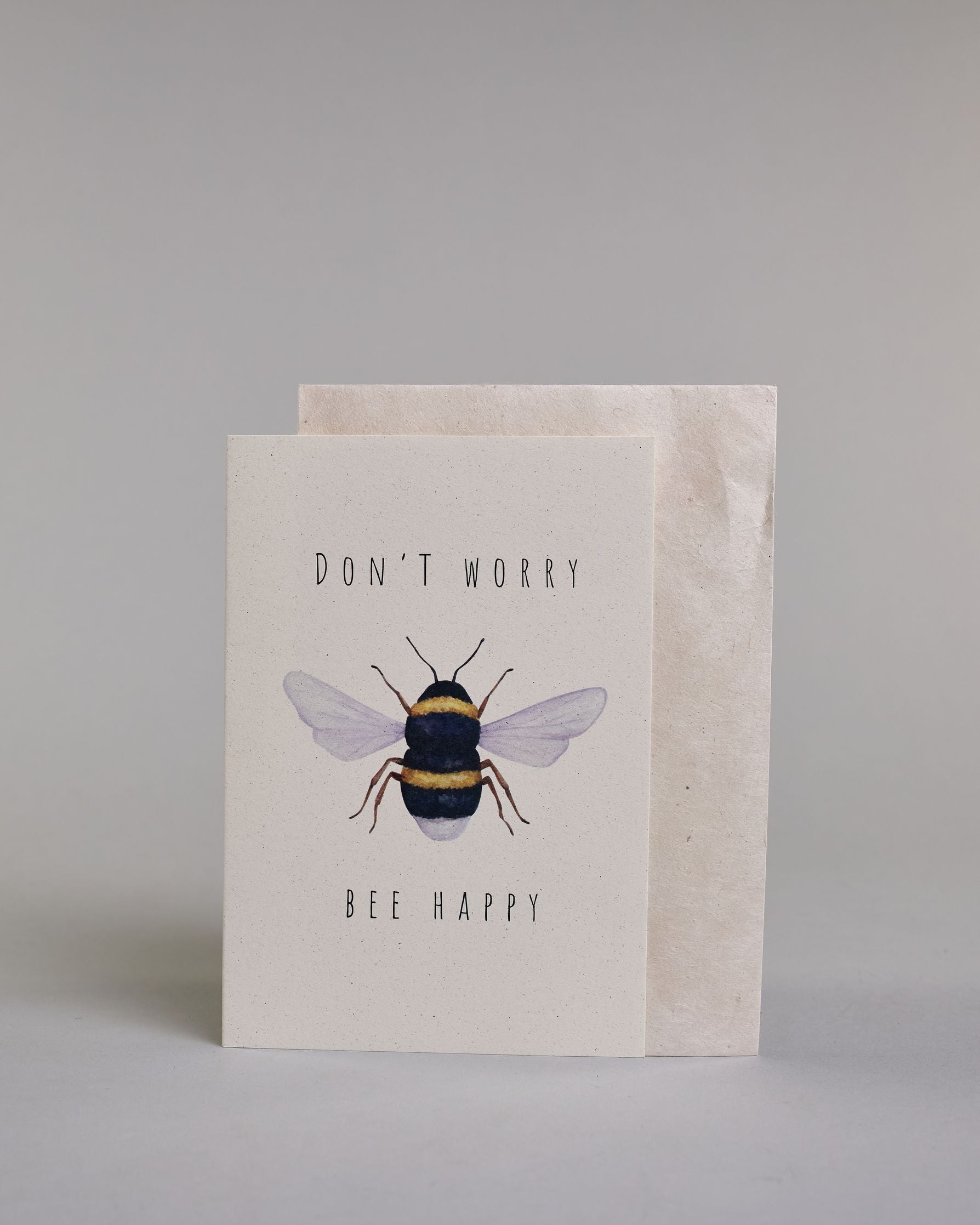 Karte auf Englisch mit der Aufschrift „Don’t worry Bee happy“ in schwarzer Schrift auf hellem Hintergrund. In der Mitte ist eine detailreich gezeichnete Biene mit gelb-schwarzem Körper und durchscheinenden Flügeln abgebildet. Dazu ein weißes handgeschöpftes Kuvert. #2