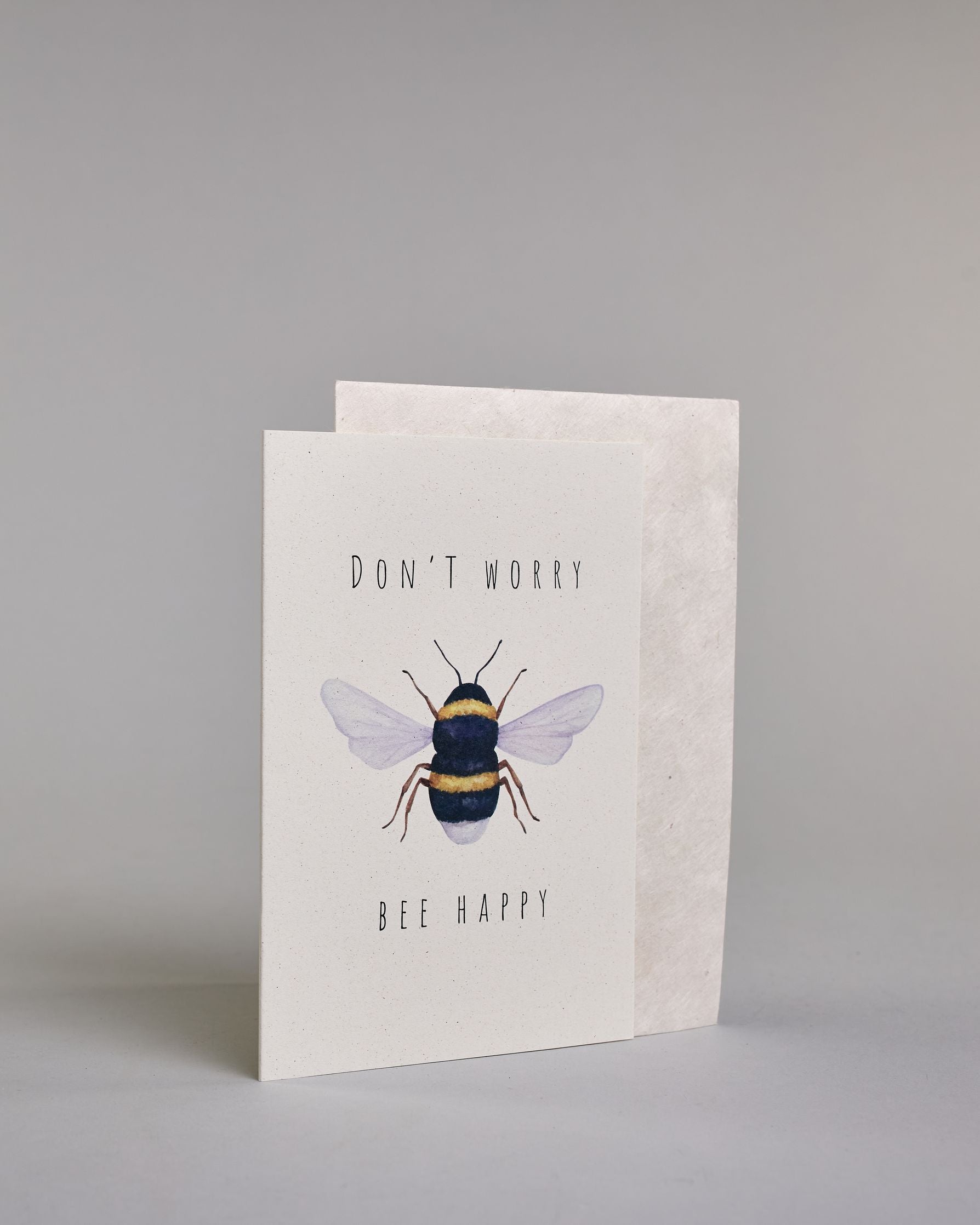Karte auf Englisch mit der Aufschrift „Don’t worry Bee happy“ in schwarzer Schrift auf hellem Hintergrund. In der Mitte ist eine detailreich gezeichnete Biene mit gelb-schwarzem Körper und durchscheinenden Flügeln abgebildet. Dazu ein weißes handgeschöpftes Kuvert. #3