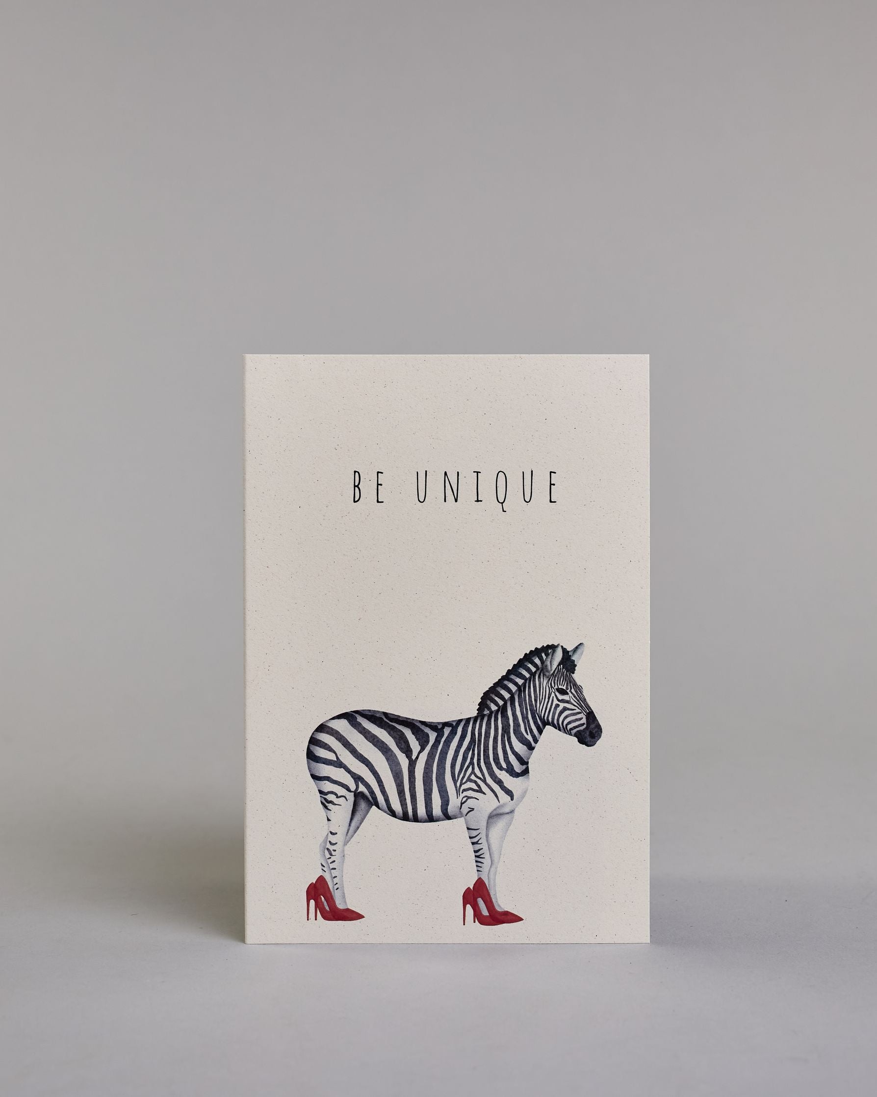 Karte in Englisch mit der Aufschrift „Be unique“ in schwarzer Schrift auf hellem Hintergrund. Darunter ist ein Zebra abgebildet, das auffällig rote High Heels trägt. Dazu ein rot-weißes handgeschöpftes Kuvert. #1