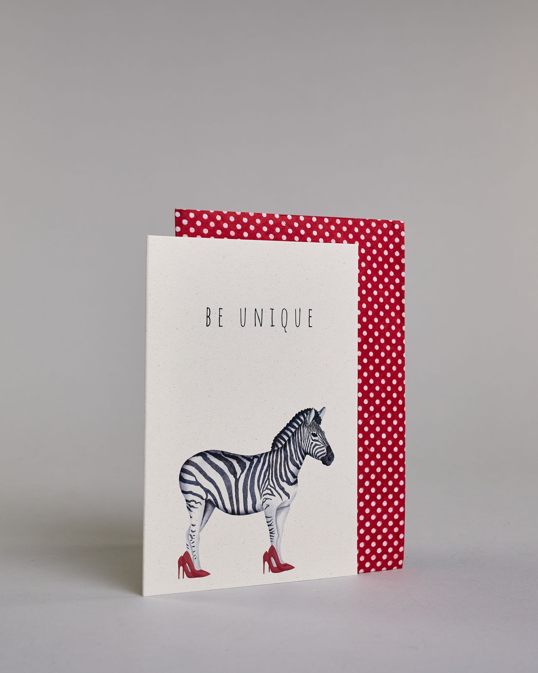 Karte in Englisch mit der Aufschrift „Be unique“ in schwarzer Schrift auf hellem Hintergrund. Darunter ist ein Zebra abgebildet, das auffällig rote High Heels trägt. Dazu ein rot-weißes handgeschöpftes Kuvert. #3