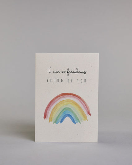 Karte mit der Aufschrift „I am so freaking proud of you“ in schwarzer Schrift auf hellem Hintergrund. Darunter ist ein bunter Regenbogen in Aquarelloptik mit den Farben Rot, Rosa, Orange, Gelb, Grün und Blau abgebildet. Dazu ein weißes handgeschöpftes Kuvert. #1