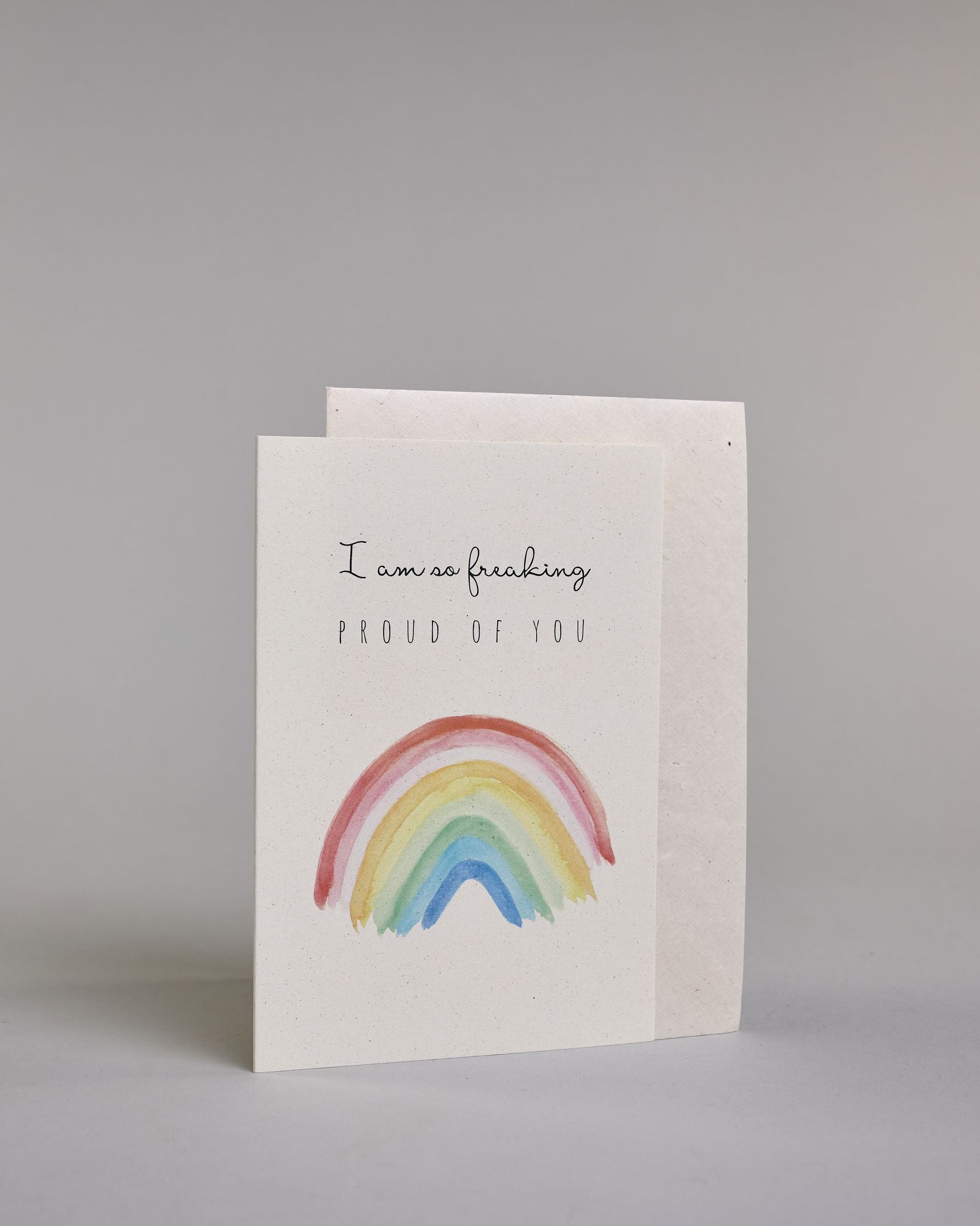 Karte mit der Aufschrift „I am so freaking proud of you“ in schwarzer Schrift auf hellem Hintergrund. Darunter ist ein bunter Regenbogen in Aquarelloptik mit den Farben Rot, Rosa, Orange, Gelb, Grün und Blau abgebildet. Dazu ein weißes handgeschöpftes Kuvert. #3