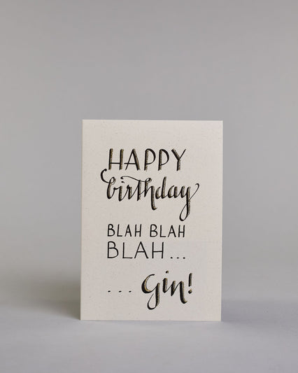Glückwunschkarte auf Englisch zum Geburtstag mit der Aufschrift "Happy birthday blah blah blah ...gin!" in schwarzer, goldakzentuierter Schrift auf hellem Hintergrund. Die Zeilen sind wiefolgt aufgeteilt: "HAPPY", darunter "birthday" beides in eher dickerer Schrift, darunter "BLAH BLAH", darunter "BLAH..." beide Zeilen in dünner gerader Kalligrafieschrift,  darunter "...Gin!" wie in geschwungener dickeren Schrift. Dazu ein grün-goldenes handgeschöpftes Kuvert. #1