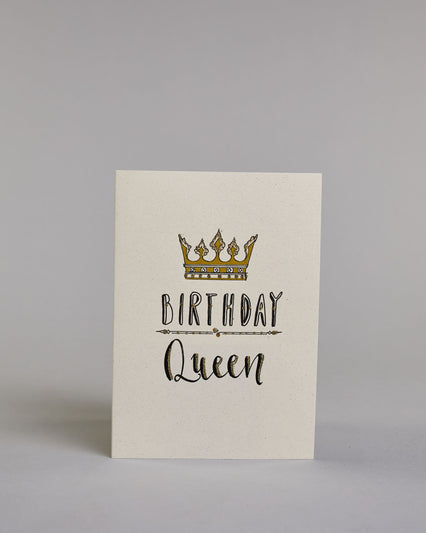 Glückwunschkarte auf Englisch zum Geburtstag mit schwarzer Kalligrafieaufschrift "Birthday Queen", mit einer prunkvollen goldenen und goldglitzernden Krone. Der Text ist übereinander geschrieben mit einer horizontalen goldverzierten Linie dazwischen. Das "Birthday" ist in Blockbuchstaben und das "Queen" in geschwungener Schreibschrift auf hellem Hintergrund. Dazu ein grün-goldenes handgeschöpftes Kuvert. #1