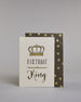 Glückwunschkarte auf Englisch zum Geburtstag mit schwarzer Kalligrafieaufschrift "Birthday King", mit einer prunkvollen goldenen und goldglitzernden Krone. Der Text ist übereinander geschrieben mit einer horizontalen goldverzierten Linie dazwischen. Das "Birthday" ist in Blockbuchstaben und das "King" in geschwungener Schreibschrift auf hellem Hintergrund. Dazu ein grün-goldenes handgeschöpftes Kuvert. #2