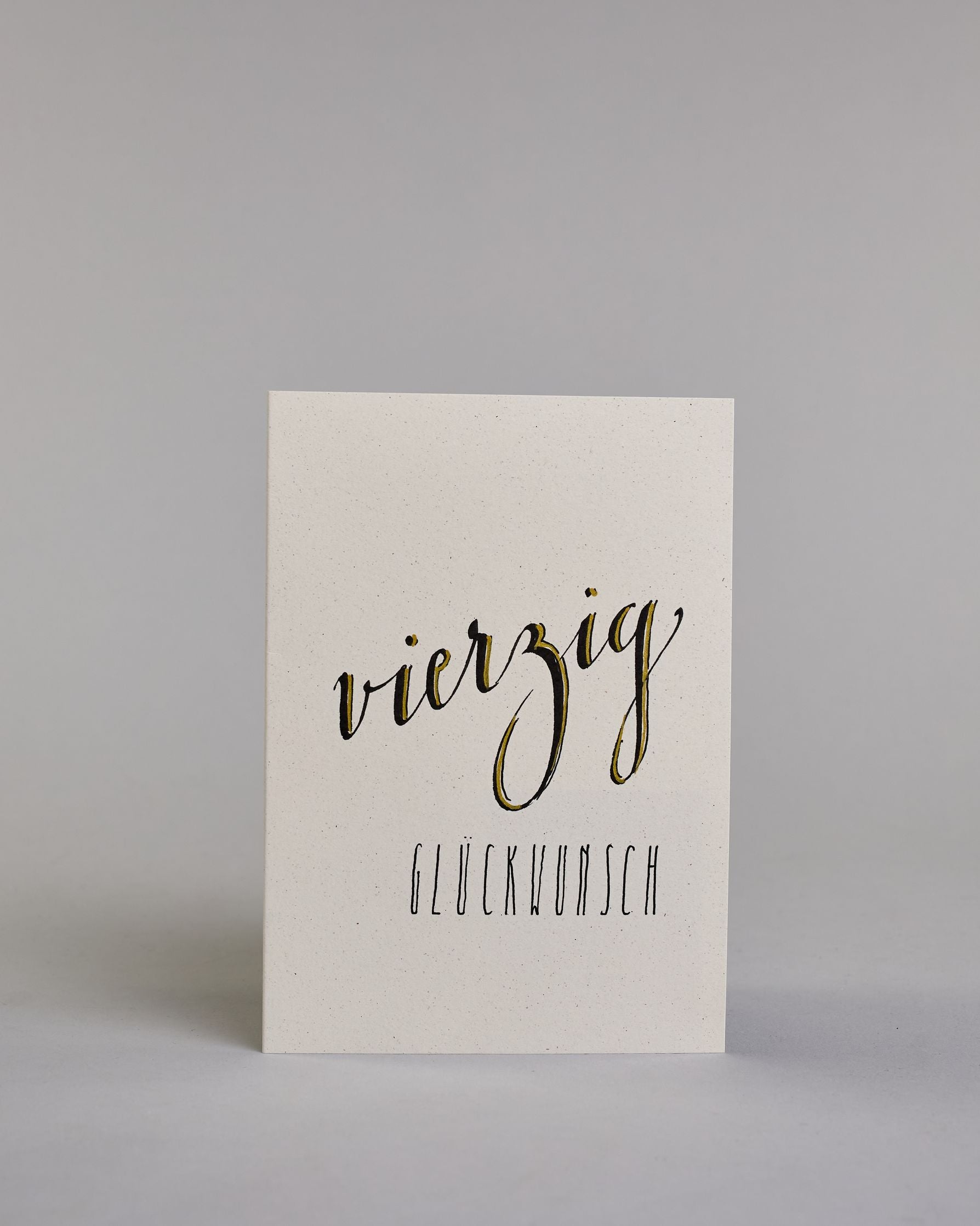 Glückwunschkarte zum Geburtstag mit schwarzer Kalligrafieaufschrift "vierzig Glückwunsch" auf hellem Hintergrund. Die ausgeschriebene Zahl ist leicht aufsteigend in geschwungener, goldverzierter Schreibschrift gestaltet und das Wort "GLÜCKWUNSCH" darunter leicht nach rechts versetzte ist in dünner, gerader Kalligrafieschrift geschrieben. Dazu ein gold-weißes handgeschöpftes Kuvert. #1