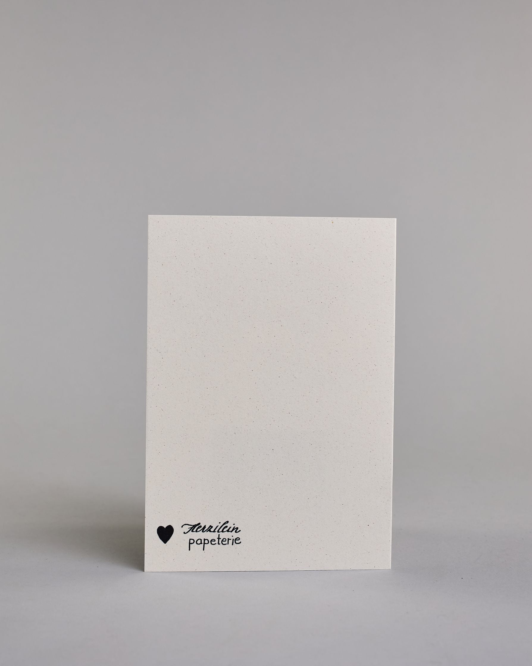 Glückwunschkarte zum Geburtstag mit schwarzer Kalligrafieaufschrift "Schon wieder 29! Happy Birthday", darunter eine gezeichnete grau, schwarz getigerte Katze die mit dem linken Auge zwinkert auf hellem Hintergrund. Der Text ist auf zwei Zeilen aufgeteilt. In der ersten steht "schon wieder 29!" in einer geschwungenen Kalligrafieschrift und darunter "HAPPY BIRTHDAY" in dünner gerader Schrift. Dazu ein weißes handgeschöpftes Kuvert. #5