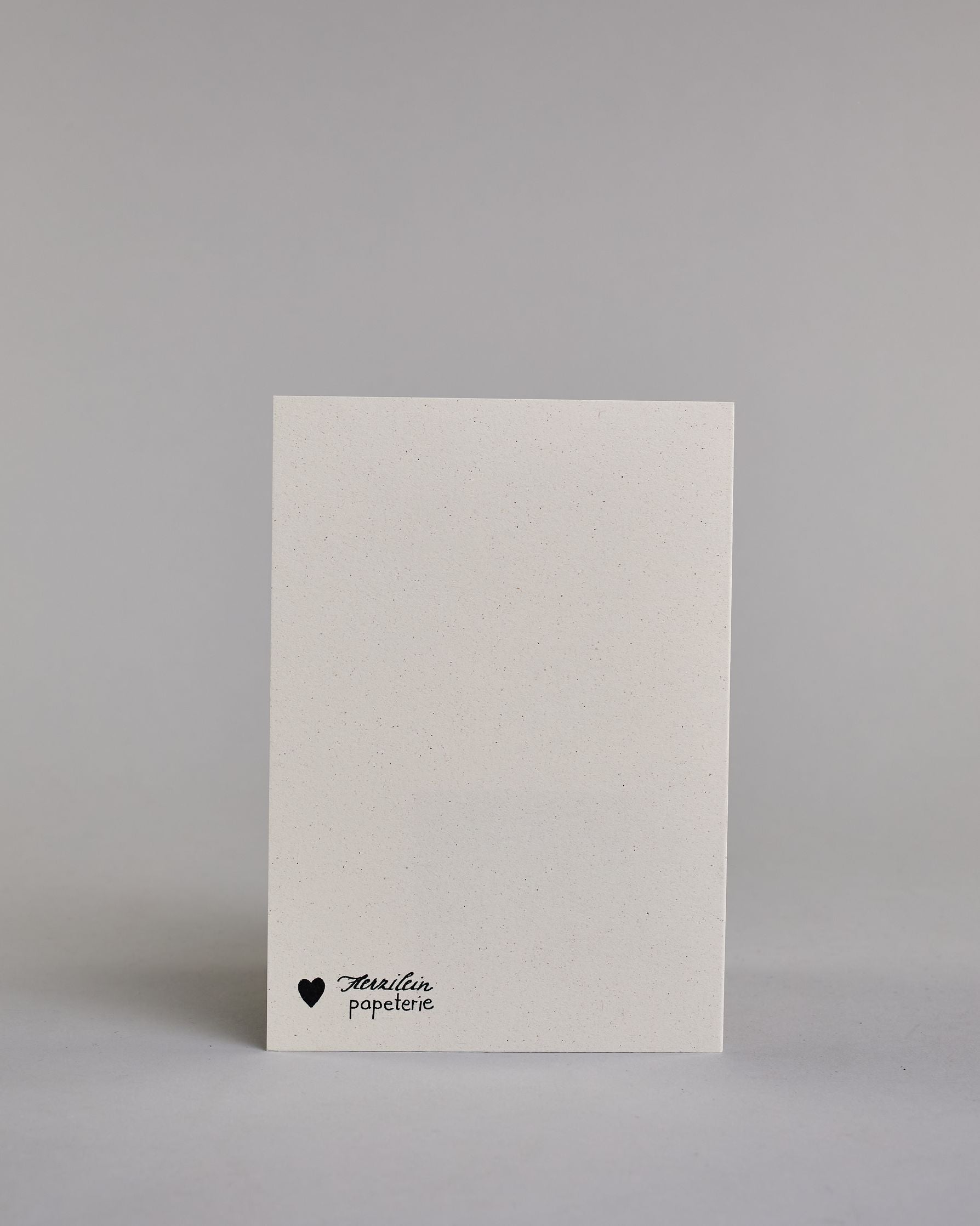 Glückwunschkarte auf Englisch zum Geburtstag mit schwarzer Kalligrafieaufschrift "cheers to many more years", mit einer gezeichneten Champagnerflasche mit goldenen Blättern als verzierung, goldenem Ettikett, goldener Flaschenhals- und Kopf und deiner blauen Masche um den Flaschenhals auf hellem Hintergrund. Oben steht in dünner geschwungener Schrift "cheers to", darunter "MANY MORE YEARS" in gerader dünner Kalligrafieschrift. Darunter kommt die falsche nach rechts geneigt von der linken Kante der Karte her…