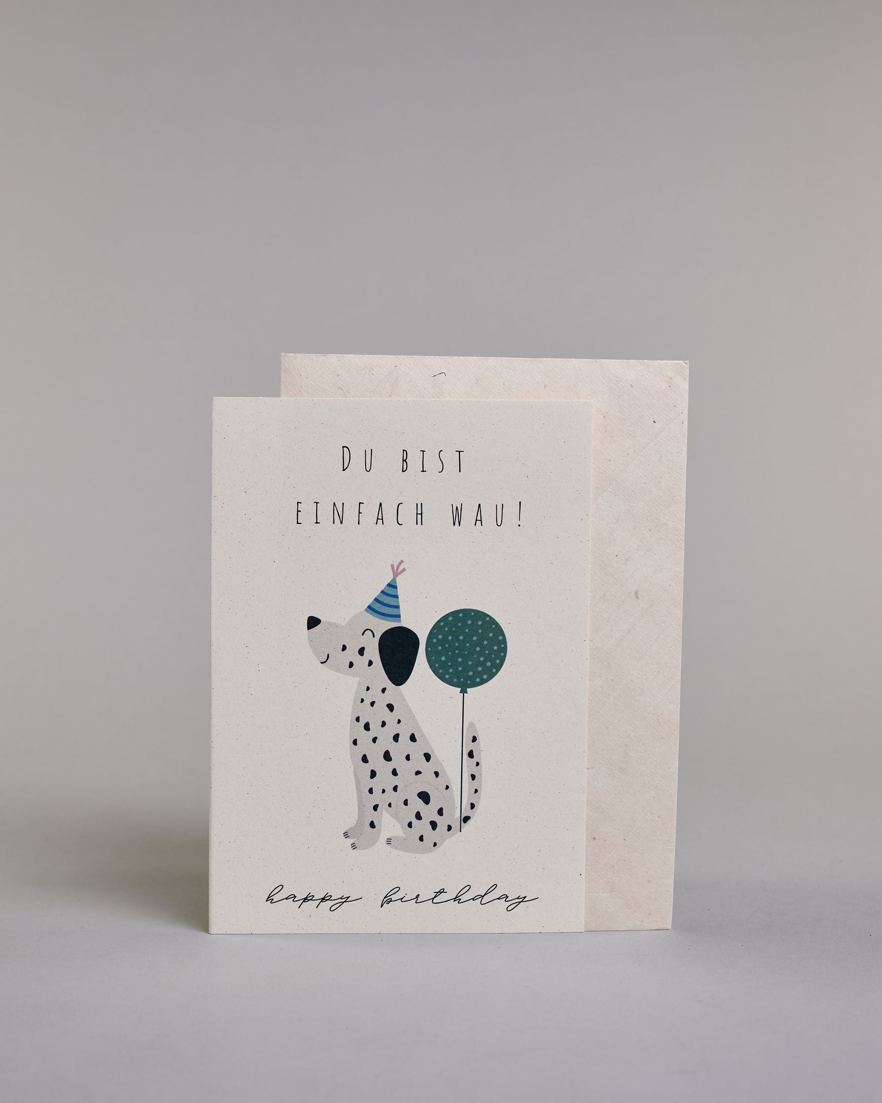 Glückwunschkarte zum Geburtstag mit schwarzer Kalligrafieaufschrift "Du bist einfach Wau! Happy Birthday", mit einem kindlich gezeichneten Dalmatiner mit blauem Partyhut an dessen Schwanz ein petrolfarbener Balon festgebunden ist auf hellem Hintergrund. Oben steht in dünner gerader Schrift "DU BIST", darunter "EINFACH WAU!", darunter ist mittig der schwarzweiß gepunktete Hund, darunter "happy birthday" in geschwungener dünner Kalligrafieschrift. Dazu ein weißes handgeschöpftes Kuvert. #2
