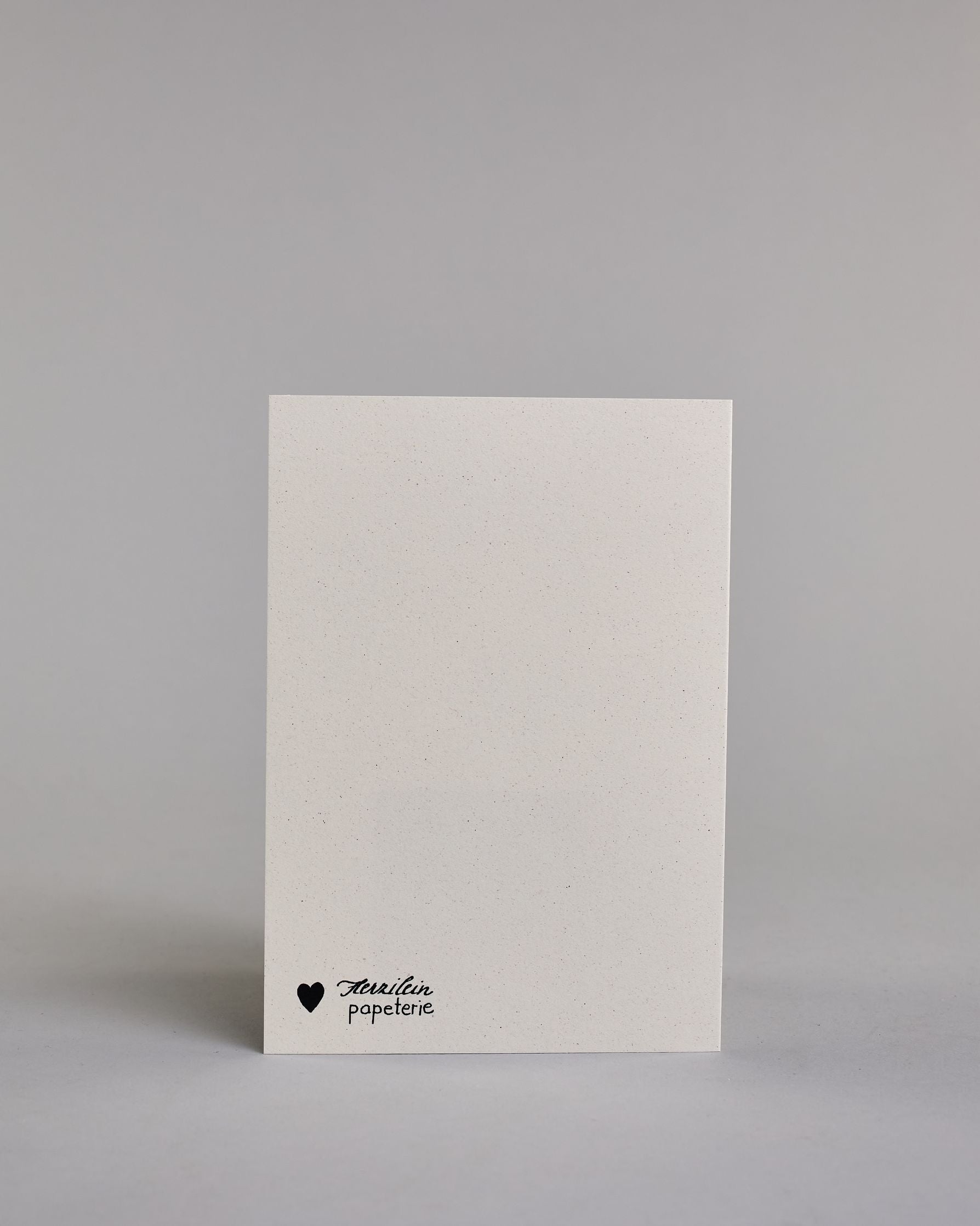 Glückwunschkarte auf Englisch zum Geburtstag mit schwarzer Kalligrafieaufschrift "We age not by years but by stories", mit zwei gezeichneten Pusteblumen deren Samen verweht werden auf hellem Hintergrund. Oben links steht in dünner gerader Schrift "WE AGE NOT", darunter "BY YEARS", darunter von links nach rechtswandernd die goldverzierte Pusteblume, darunter rechts "BUT BY STORIES" in gerader dünner Kalligrafieschrift. Dazu ein weißes handgeschöpftes Kuvert. #4