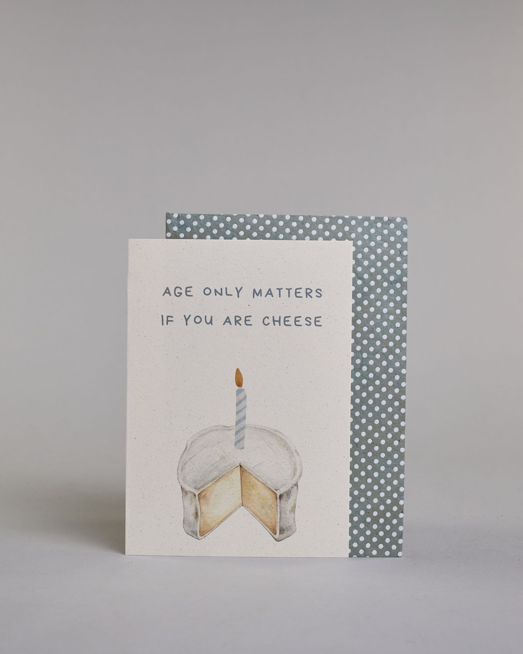 Glückwunschkarte auf Englisch zum Geburtstag mit blauer Kalligrafieaufschrift "age only matters if you are cheese", mit einem genzeichnetem Camembert in dem eine blau gestreifte Kerze steckt auf hellem Hintergund. Oben steht in zwei Zeilen "AGE ONLY MATTERS", darunter "IF YOU ARE CHEESE" beides in Blockbuchstaben und darunter mittig der Käse. Dazu ein blau-weißes handgeschöpftes Kuvert. #2