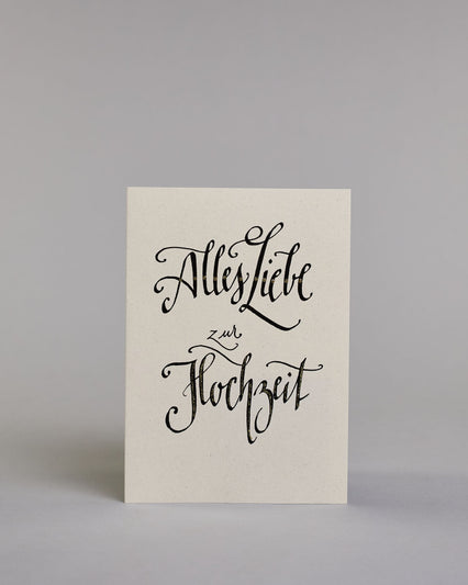 Glückwunschkarte zur Hochzeit mit der Kalligrafieaufschrift "Alles Liebe zur Hochzeit" auf hellem Hintergrund. Die Schrift ist mit feinen goldfarbenen Akzenten versehen. Das Wort „zur“ ist kleiner gesetzt und steht zwischen den beiden großen Wörtern „Liebe“ und „Hochzeit“. Dazu ein gold-weißes handgeschöpftes Kuvert. #1