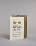Glückwunschkarte auf Englisch zur Hochzeit für zwei Männer mit der Kalligrafieaufschrift "Two Kings make a pair congratulations" auf hellem Hintergrund. Sie zeigt oben zwei Kronen welche mit Gold verziert sind. Darunter steht in großer, geschwungener schwarzer Schrift mit goldenen Details „Two kings“, darunter mit dünner Kalligraphieschrift "MAKE A PAIR". Unterhalb davon befindet sich in ebenfalls gerader schwarzer Schrift "CONGRATULATIONS" welches sowohl ober- als auch unterhalb prunkvolle horizotale Lini…
