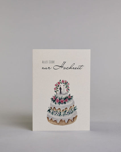 Glückwunschkarte zur Hochzeit mit schwarzer Kalligrafieaufschrift "Alles Liebe zur Hochzeit", darunter eine dreistückige Hochzeitstorte mit rosanen und weißen Blumen geschmückt und einem Brautpaar unter einem Hochzeitsbogen auf der obersten Tortenebene. Der Text "ALLES LIEBE" ist in dünner schwarzer Kalligraphieschrift, darunter das "zur Hochzeit" in geschwungener schwarzer Schreibschrift und alles ist auf hellem Hintergrund. Dazu ein weißes handgeschöpftes Kuvert. #1