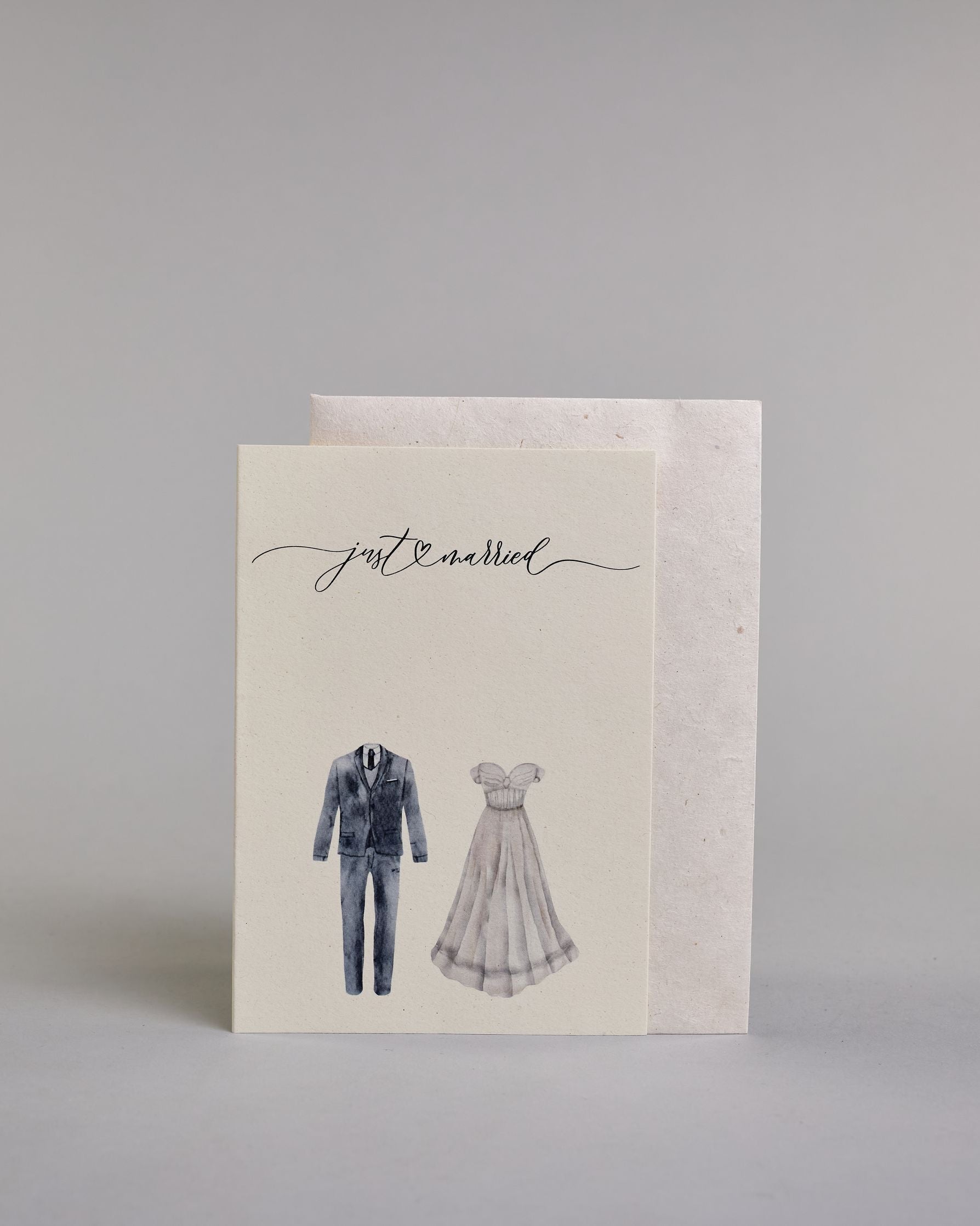 Glückwunschkarte auf Englisch zur Hochzeit mit schwarzer Kalligrafieaufschrift "just married", darunter ein schwarzer Anzug und rechts daneben ein weißes Hochzeitskleid. Der Text "just married" ist in geschwungener schwarzer Kalligraphieschrift und zieht sich von ganz links nach ganz rechts über die Karte, außerdem befindet sich im Schwung der Schrift in der Mitte der beiden Worte ein Herz und alles ist auf hellem Hintergrund. Dazu ein weißes handgeschöpftes Kuvert. #2