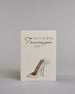 Klappkarte mit der Aufschrift "Willst du meine Trauzeugin sein?" in schwarzer Schrift auf hellem Hintergrund. Darunter ist ein eleganter weißer High Heel mit einer großen Schleife an der Ferse abgebildet. Der Text ist in drei Zeilen verfasst. "WILLST DU" ist in dünner schwarzer Kalligraphieschrift über dem Wort "Trauzeugin", welches in großer geschwungener Schreibschrift gestaltet ist, dargestellt. Darunter ist in ebenfalls dünner Kalligrafieschrift "SEIN?". Alles ist auf hellem Hintergrund und dazu kommt…