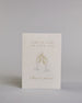 Glückwunschkarte zur Hochzeit mit hellbrauner Kalligrafieaufschrift "Hand in Hand ein Leben lang cheers to forever!". Die Karte ist wiefolgt gegliedert: "HAND IN HAND", darunter "EIN LEBEN LANG", beide Zeilen sind in einer dünnen aufrechten Kalligrafieschrift gestaltet. Darunter stoßen zwei gezeichnete Champagnergläser an, um dessen Gläserhälsen jeweils eine weiße Schleife gebunden ist. Der Champagner schwapt durch den Schwung etwas über den Glasrand und ist mit Golddeteils verfeinert. Darunter ist in gesc…