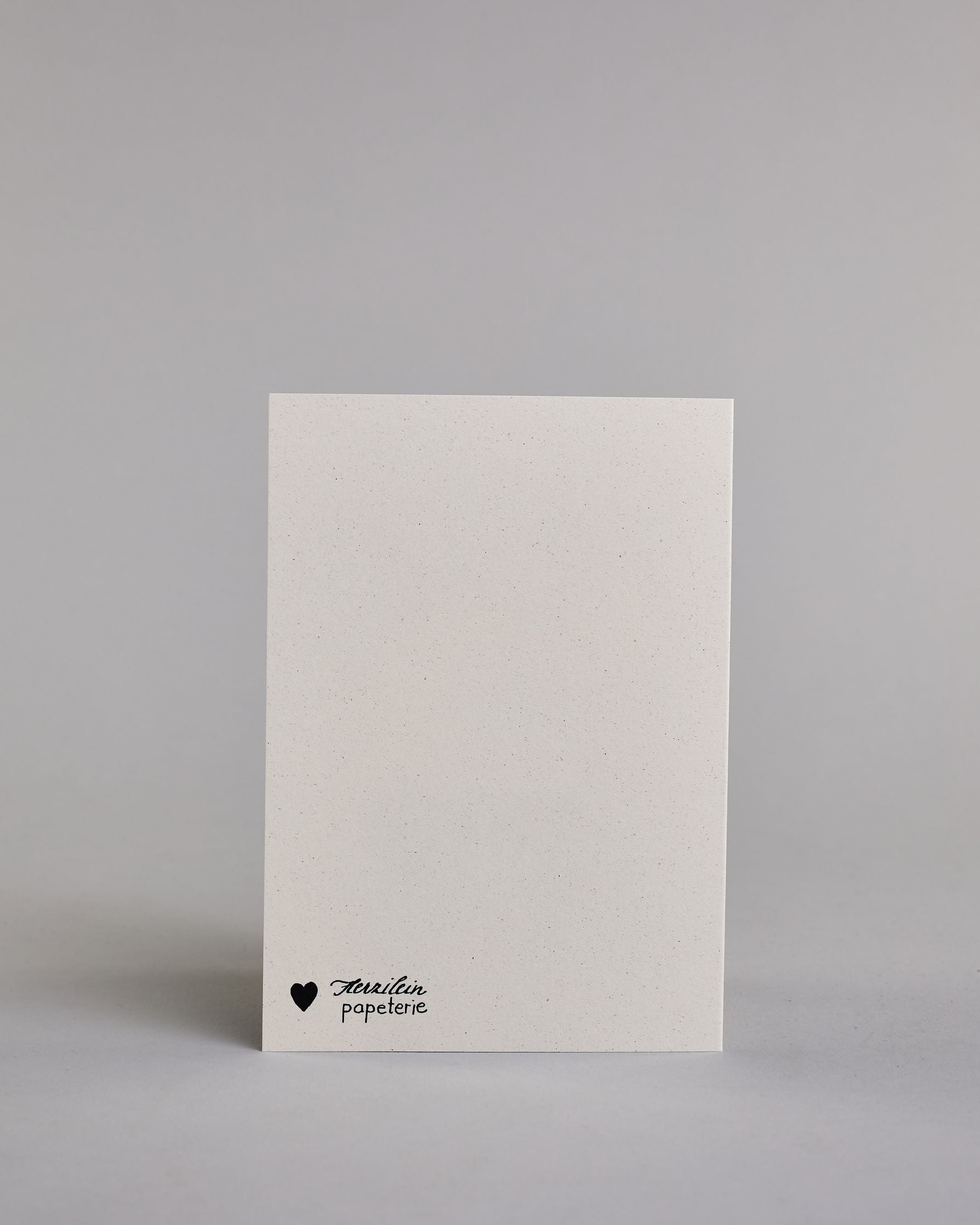 Glückwunschkarte zur Hochzeit mit hellbrauner Kalligrafieaufschrift "Hand in Hand ein Leben lang cheers to forever!". Die Karte ist wiefolgt gegliedert: "HAND IN HAND", darunter "EIN LEBEN LANG", beide Zeilen sind in einer dünnen aufrechten Kalligrafieschrift gestaltet. Darunter stoßen zwei gezeichnete Champagnergläser an, um dessen Gläserhälsen jeweils eine weiße Schleife gebunden ist. Der Champagner schwapt durch den Schwung etwas über den Glasrand und ist mit Golddeteils verfeinert. Darunter ist in gesc…