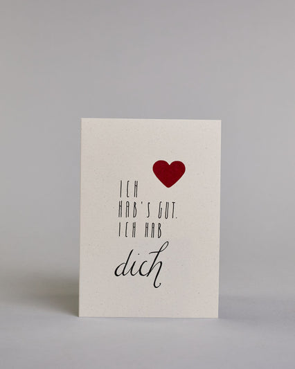 Klappkarte für Liebende mit schwarzer Kalligrafieaufschrift "Ich hab's gut. Ich hab dich" mit einem rotem aufgeklebtem Herz auf hellem Hintergrund. Die Schrift ist auf 4 Zeilen aufgeteilt. "ICH", darunter "HAB'S GUT.", darunter "ICH HAB" alles in einer dünnen geraden Kalligrafieschrift, darunter "dich" in einer geschwungenen Schreibschrift. Die Schrift ist eher linksbündig, das Herz klebt auf Höhe der ersten Zeile, mit dem "ICH" rechts auf der Karte.  Dazu ein rot-weißes handgeschöpftes Kuvert. #1