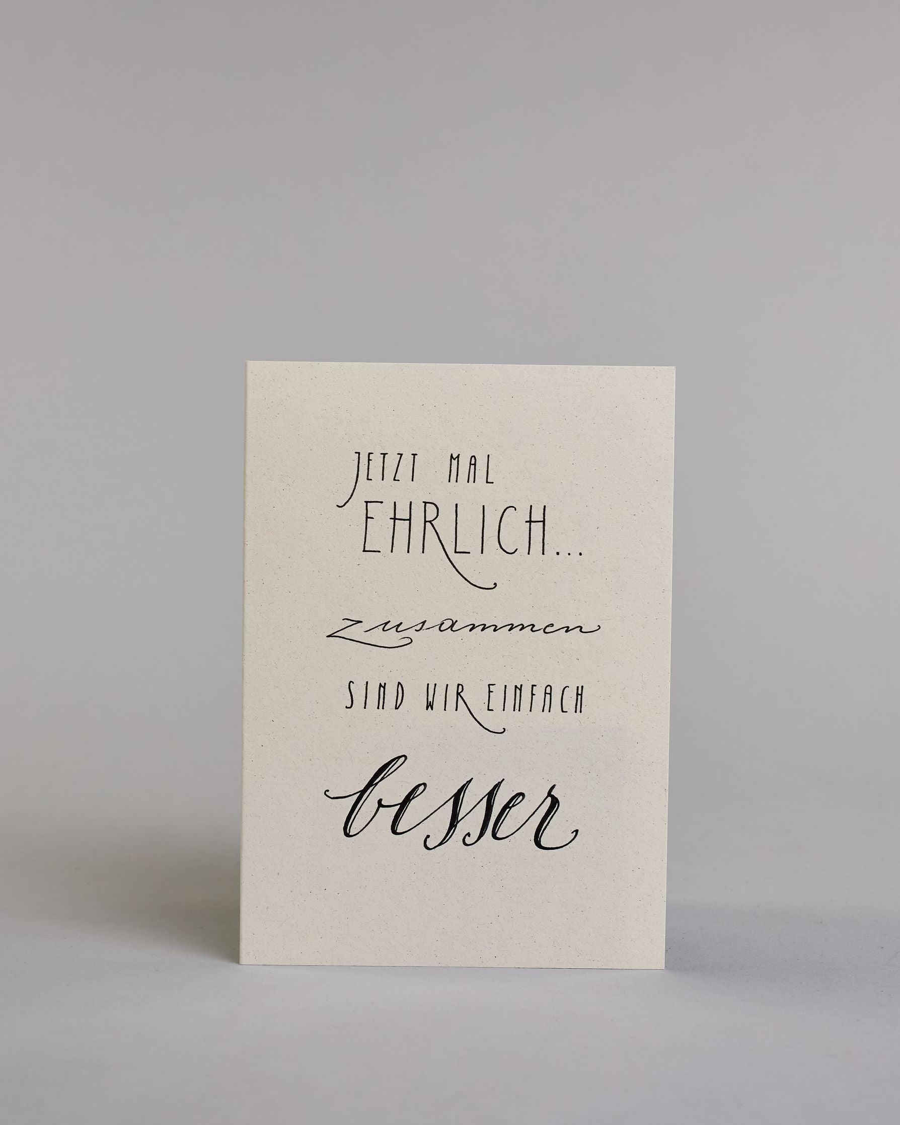 Klappkarte für Liebende mit schwarzer Kalligrafieaufschrift "Jetzt mal ehrlich... zusammen sind wir einfach besser" auf hellem Hintergrund. Die Zeilen gliedern sich wiefolgt: "JETZT MAL", darunter "EHRLICH...", in dünner, geraden Kalligrafieschrift, darunter "zusammen" in geschwungener Schreibschrift, darunter "SIND WIR EINFACH" wieder in dünner gerader Schrift und darunter "besser" wieder geschwungen geschrieben. Dazu ein gold-weißes handgeschöpftes Kuvert. #1
