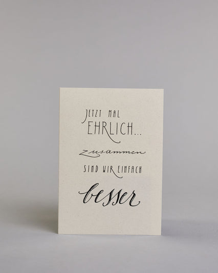 Klappkarte für Liebende mit schwarzer Kalligrafieaufschrift "Jetzt mal ehrlich... zusammen sind wir einfach besser" auf hellem Hintergrund. Die Zeilen gliedern sich wiefolgt: "JETZT MAL", darunter "EHRLICH...", in dünner, geraden Kalligrafieschrift, darunter "zusammen" in geschwungener Schreibschrift, darunter "SIND WIR EINFACH" wieder in dünner gerader Schrift und darunter "besser" wieder geschwungen geschrieben. Dazu ein gold-weißes handgeschöpftes Kuvert. #1