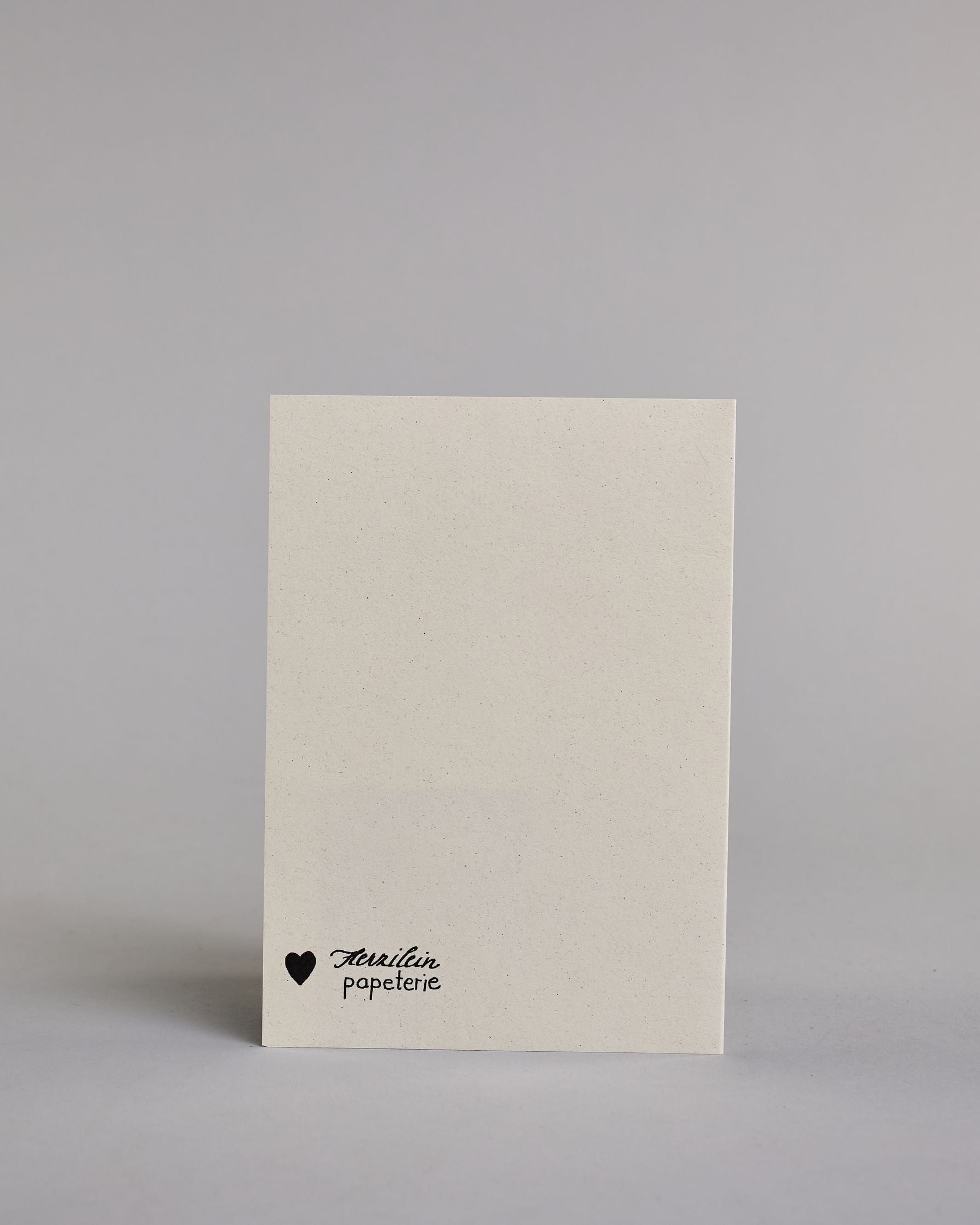 Klappkarte für Liebende mit schwarzer Kalligrafieaufschrift "Bleib noch ein bisschen... Wie lange? Ein Leben!" auf hellem Hintergrund. Der Text ist auf vier Zeilen mit jeweils immer zwei Worten auf geteilt. Die Zeilen "bleib noch", "ein bisschen" und "ein Leben!" sind in dünner geschwungener Schreibschrift gestaltet, während "WIE LANGE?" in dünner, gerader Kalligrafieschrift geschrieben ist. Dazu ein grün-goldenes handgeschöpftes Kuvert. #4