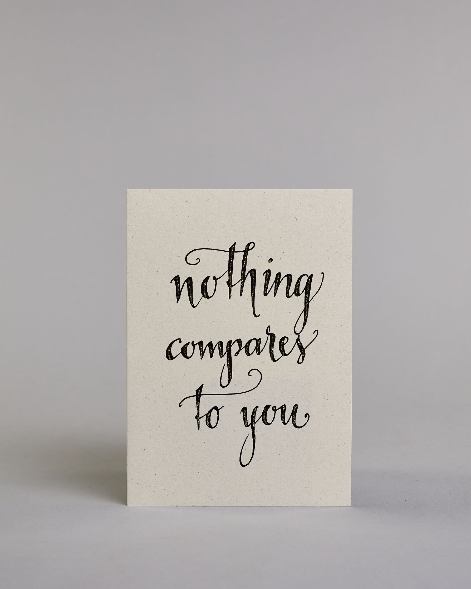 Klappkarte für Liebende auf Englisch mit schwarzer Kalligrafieaufschrift "Nothing compares to you" auf hellem Hintergrund. Der Text ist in folgende drei Zeilen aufgeteilt: "nothing", darunter "compares", darunter "to you", alles ist mit Goldglitzer verziert und in geschwungener Schreibschrift gestaltet. Dazu ein grün-goldenes handgeschöpftes Kuvert. #1