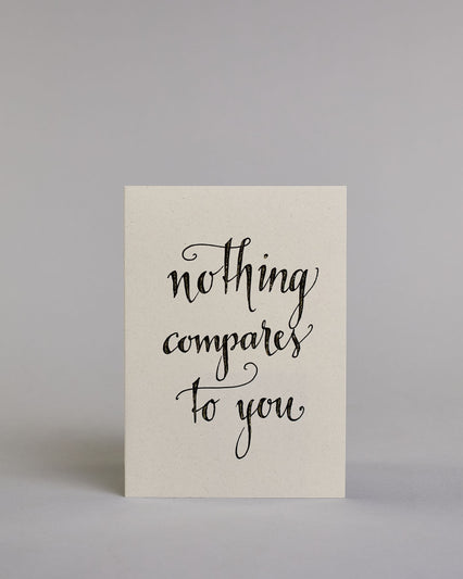 Klappkarte für Liebende auf Englisch mit schwarzer Kalligrafieaufschrift "Nothing compares to you" auf hellem Hintergrund. Der Text ist in folgende drei Zeilen aufgeteilt: "nothing", darunter "compares", darunter "to you", alles ist mit Goldglitzer verziert und in geschwungener Schreibschrift gestaltet. Dazu ein grün-goldenes handgeschöpftes Kuvert. #1