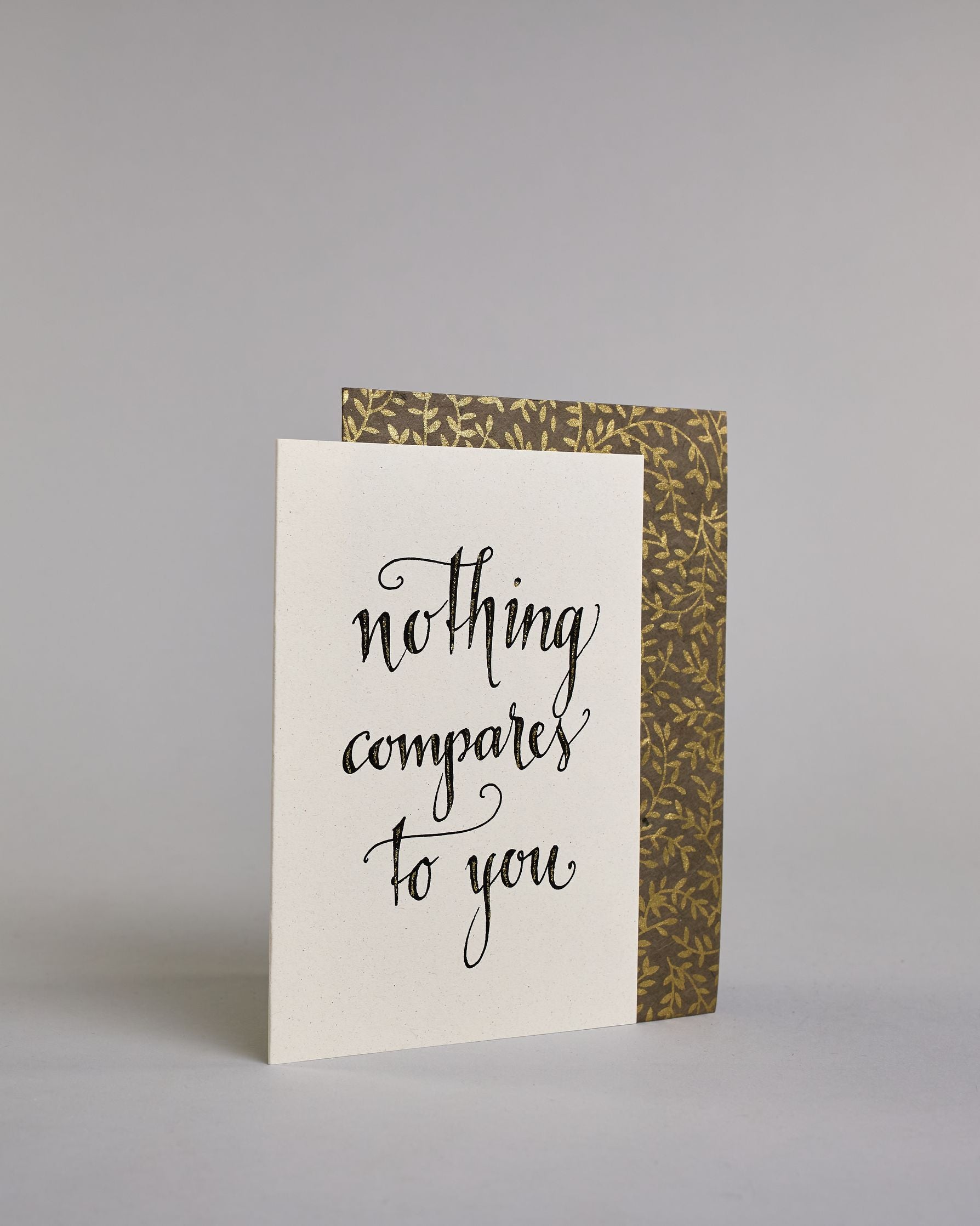 Klappkarte für Liebende auf Englisch mit schwarzer Kalligrafieaufschrift "Nothing compares to you" auf hellem Hintergrund. Der Text ist in folgende drei Zeilen aufgeteilt: "nothing", darunter "compares", darunter "to you", alles ist mit Goldglitzer verziert und in geschwungener Schreibschrift gestaltet. Dazu ein grün-goldenes handgeschöpftes Kuvert. #3