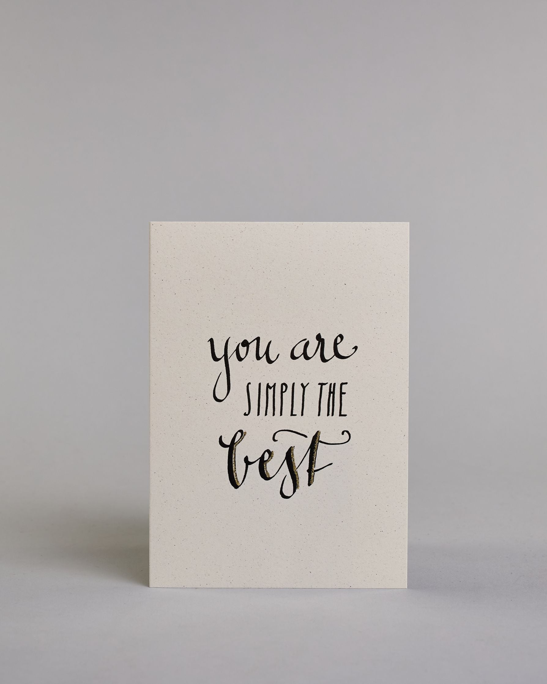 Klappkarte für Liebende auf Englisch mit schwarzer Kalligrafieaufschrift "You are simply the best" auf hellem Hintergrund. Der Text ist in folgende drei Zeilen aufgeteilt: "you are" in geschwungener Schreibschrift, darunter "SIMPLY THE" in gerader dünner Kalligrafieschrift, darunter "best" in der gleichen geschwungenen Schreibschrift wie in der ersten Zeile. Dazu ein grün-goldenes handgeschöpftes Kuvert. #1
