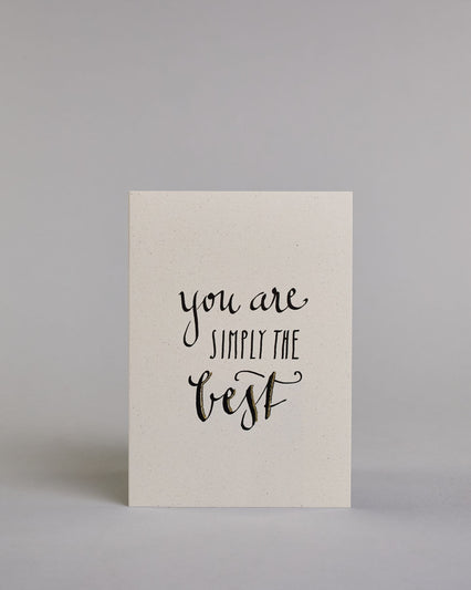 Klappkarte für Liebende auf Englisch mit schwarzer Kalligrafieaufschrift "You are simply the best" auf hellem Hintergrund. Der Text ist in folgende drei Zeilen aufgeteilt: "you are" in geschwungener Schreibschrift, darunter "SIMPLY THE" in gerader dünner Kalligrafieschrift, darunter "best" in der gleichen geschwungenen Schreibschrift wie in der ersten Zeile. Dazu ein grün-goldenes handgeschöpftes Kuvert. #1