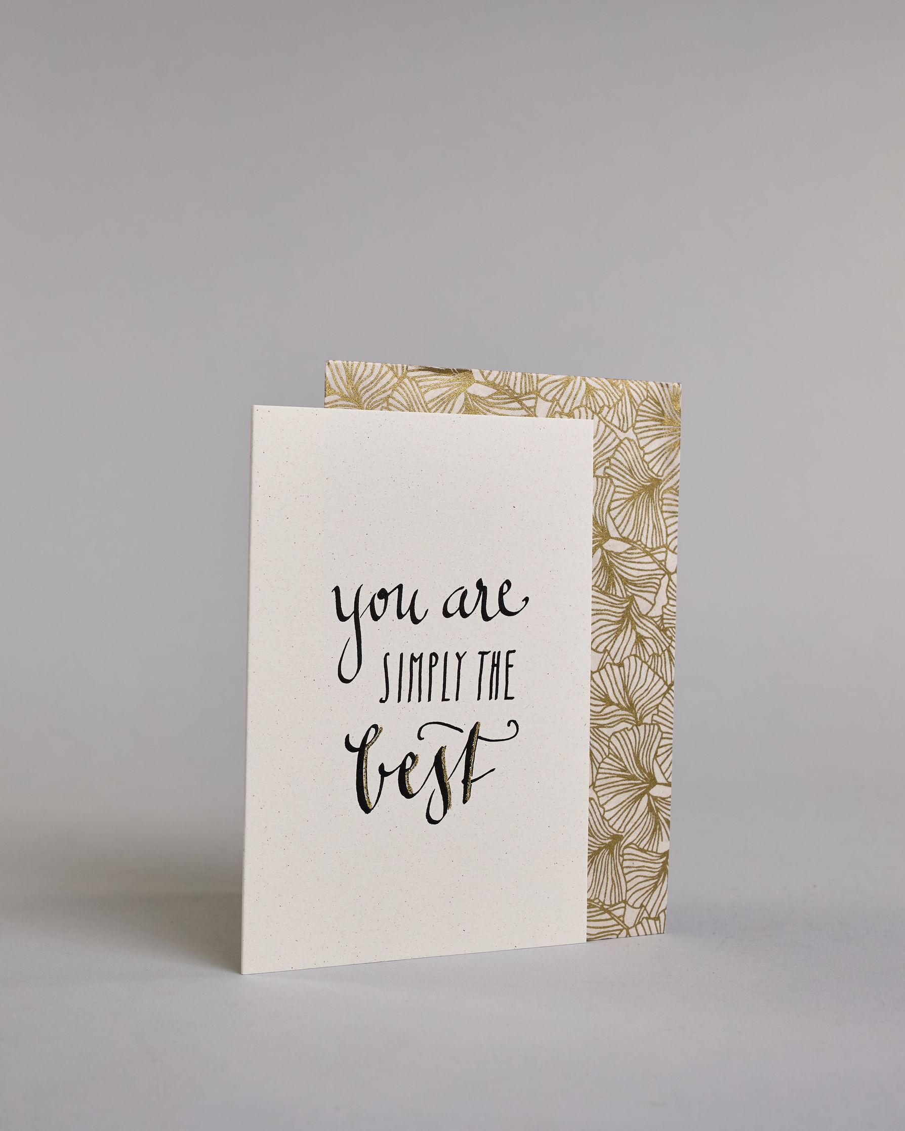 Klappkarte für Liebende auf Englisch mit schwarzer Kalligrafieaufschrift "You are simply the best" auf hellem Hintergrund. Der Text ist in folgende drei Zeilen aufgeteilt: "you are" in geschwungener Schreibschrift, darunter "SIMPLY THE" in gerader dünner Kalligrafieschrift, darunter "best" in der gleichen geschwungenen Schreibschrift wie in der ersten Zeile. Dazu ein grün-goldenes handgeschöpftes Kuvert. #3