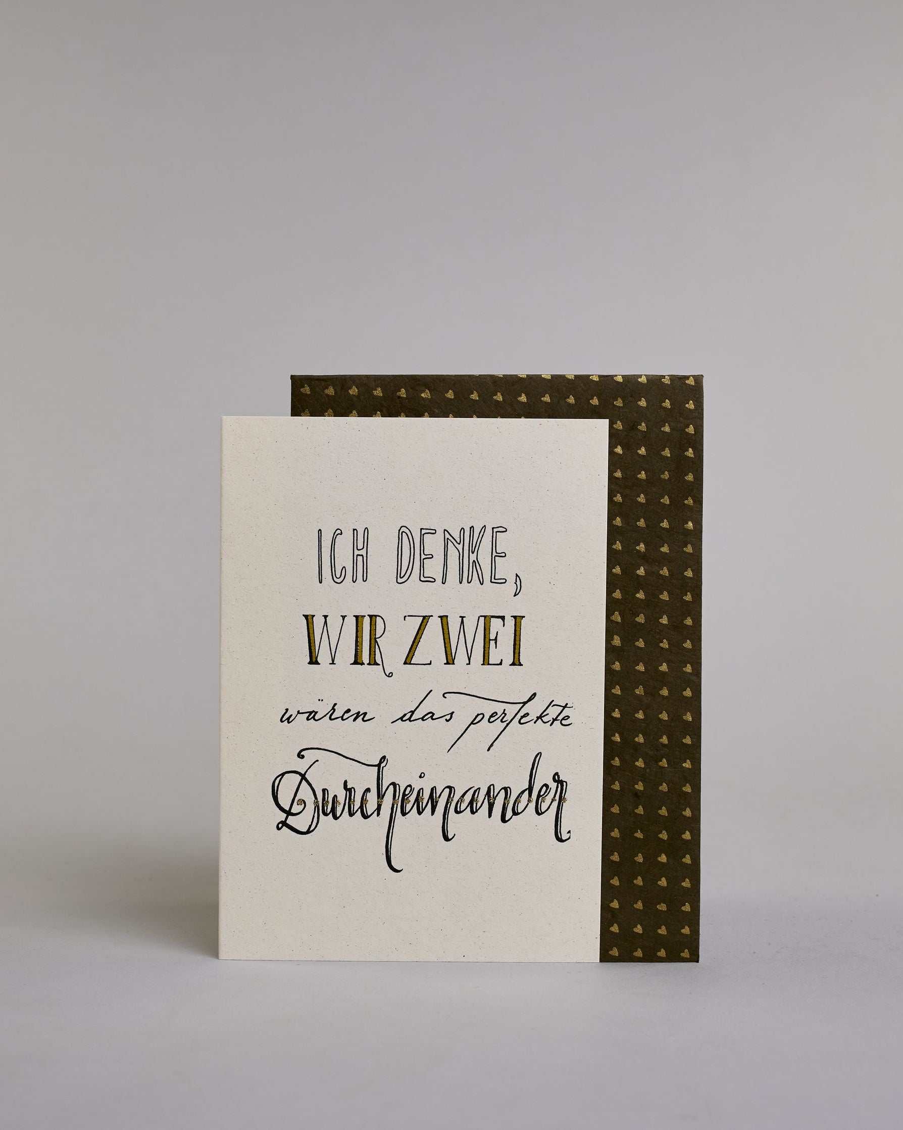Klappkarte für Liebende mit schwarzer Kalligrafieaufschrift "Ich denke wir zwei wären das perfekte Durcheinander" auf hellem Hintergrund. Der Text ist in folgende vier Zeilen aufgeteilt: "ICH DENKE," in dicken geraden Kalligrafieschrift die weiß ausgemalt ist, darunter "WIR ZWEI" in einer geraden Kalligrafieschrift, darunter "wären das perfekte" in einer dünnen kleinen Schreibschrift, darunter "Durcheinander" in einer größeren Schreibschrift gestaltet . Dazu ein weiß-goldenes handgeschöpftes Kuvert. #2