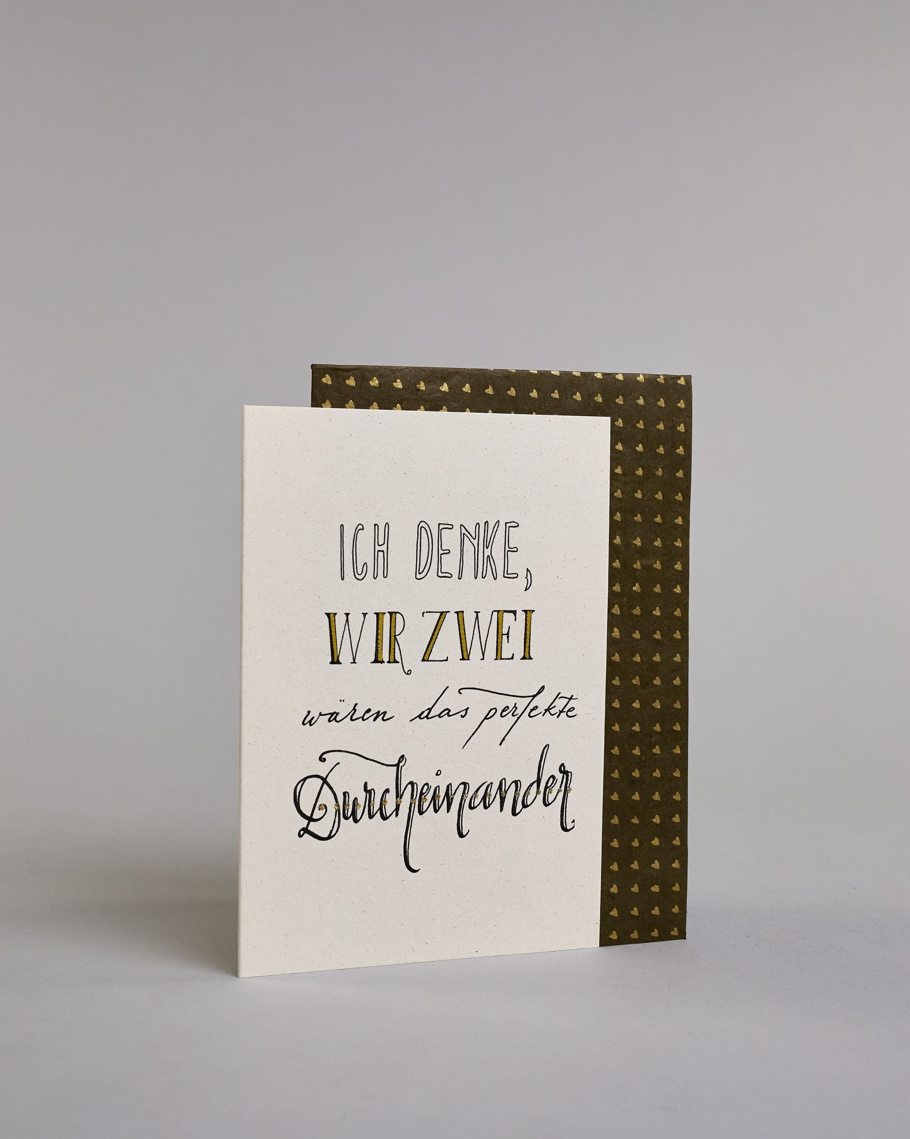 Klappkarte für Liebende mit schwarzer Kalligrafieaufschrift "Ich denke wir zwei wären das perfekte Durcheinander" auf hellem Hintergrund. Der Text ist in folgende vier Zeilen aufgeteilt: "ICH DENKE," in dicken geraden Kalligrafieschrift die weiß ausgemalt ist, darunter "WIR ZWEI" in einer geraden Kalligrafieschrift, darunter "wären das perfekte" in einer dünnen kleinen Schreibschrift, darunter "Durcheinander" in einer größeren Schreibschrift gestaltet . Dazu ein weiß-goldenes handgeschöpftes Kuvert. #3