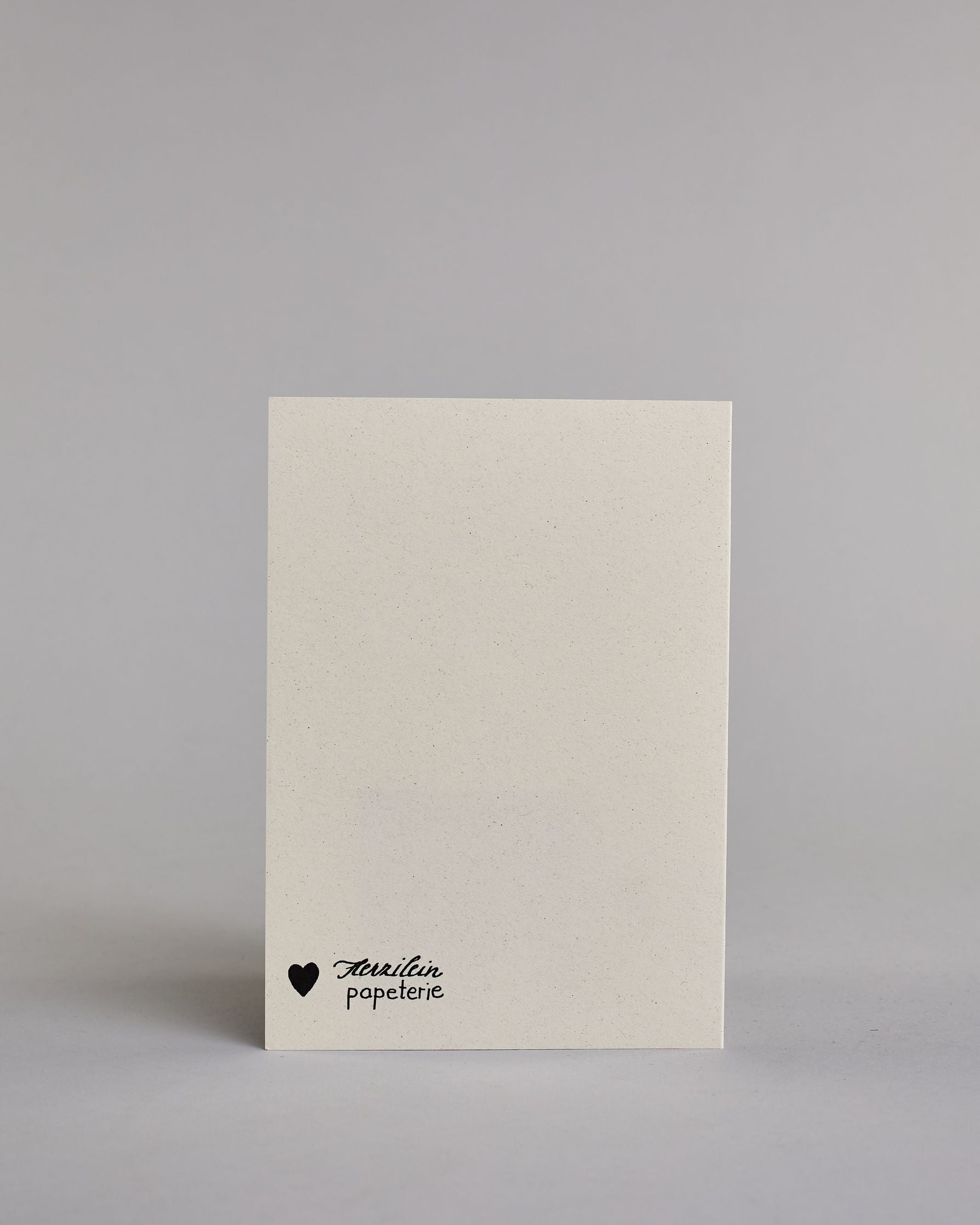 Klappkarte für Liebende mit schwarzer Kalligrafieaufschrift "Herzensmensch" mit drei gezeichneten schwebenden Herzen auf hellem Hintergrund. Der Text ist in zwei Zeilen aufgeteilt: "HERZENS" in schwarzer dicker, gerader Kalligrafieschrift, gold verziert und darunter "MENSCH" in verglitzerter Schreibschrift gestaltet, die Herzen befinden sich links über der ersten Zeile, rechts zwischen den beiden Zeilen und recht mittig unter der zweiten Zeile und sie sind gold bemalt. Dazu ein gold-weißes handgeschöpftes…