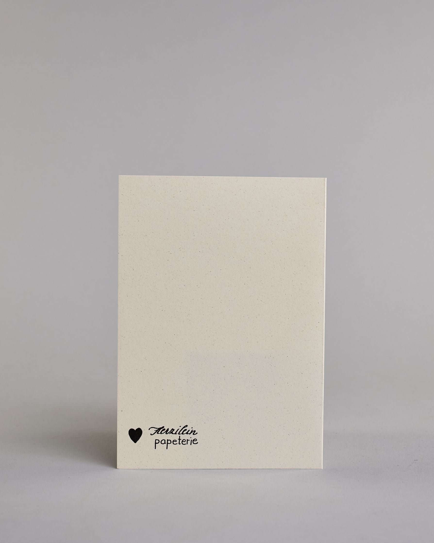 Klappkarte für Liebende mit schwarzer Kalligrafieaufschrift "Ich seh' dich an und bin Zuhause" auf hellem Hintergrund. Der Text ist in folgende drei Zeilen aufgeteilt: "ICH SEH' DICH AN", darunter "UND BIN" beide Zeilen sind in einer verspielten geraden Kalligrafieschrift gestaltet, darunter "Zuhause" in verspielter geschwungener Schreibschrift. Dazu ein handgeschöpftes Kuvert. #4