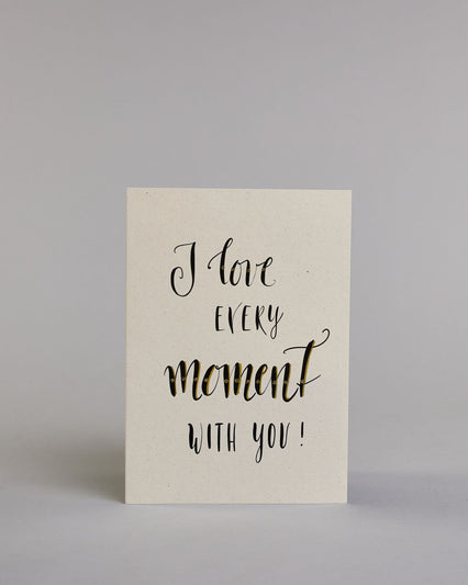 Klappkarte für Liebende in Englisch mit schwarzer Kalligrafieaufschrift "I love every moment with you!" auf hellem Hintergrund. Der Text ist in folgende vier Zeilen aufgeteilt: "I love" in verschnörkelter Schreibschrift mit glitzernden Punkten auf dem Wort "love", darunter "EVERY" in verspielter gerader Kalligrafieschrift, darunter "moment" größer gehalten in einer dickeren Schreibschrift, darunter "with you!" in der gleichen Schrift wie das Wort "EVERY". Dazu ein grün-goldenes handgeschöpftes Kuvert. #1