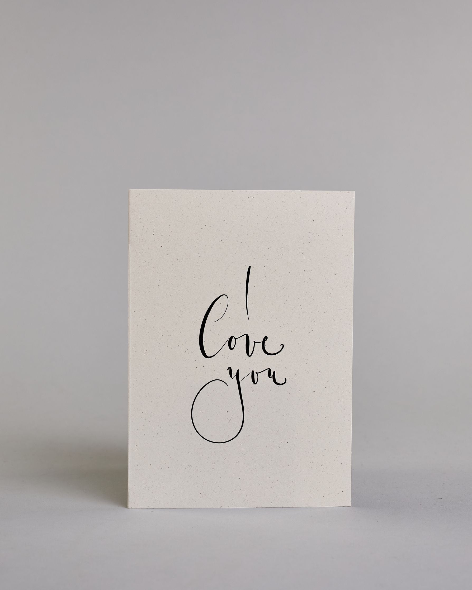 Klappkarte für Liebende in Englisch mit schwarzer Kalligrafieaufschrift "I love you" auf hellem Hintergrund. Der Text ist in drei Zeilen mit jeweils einem Wort aufgeteilt und in einer kunstvollen Schreibschrif gestaltet. Dazu ein grün-goldenes handgeschöpftes Kuvert. #1