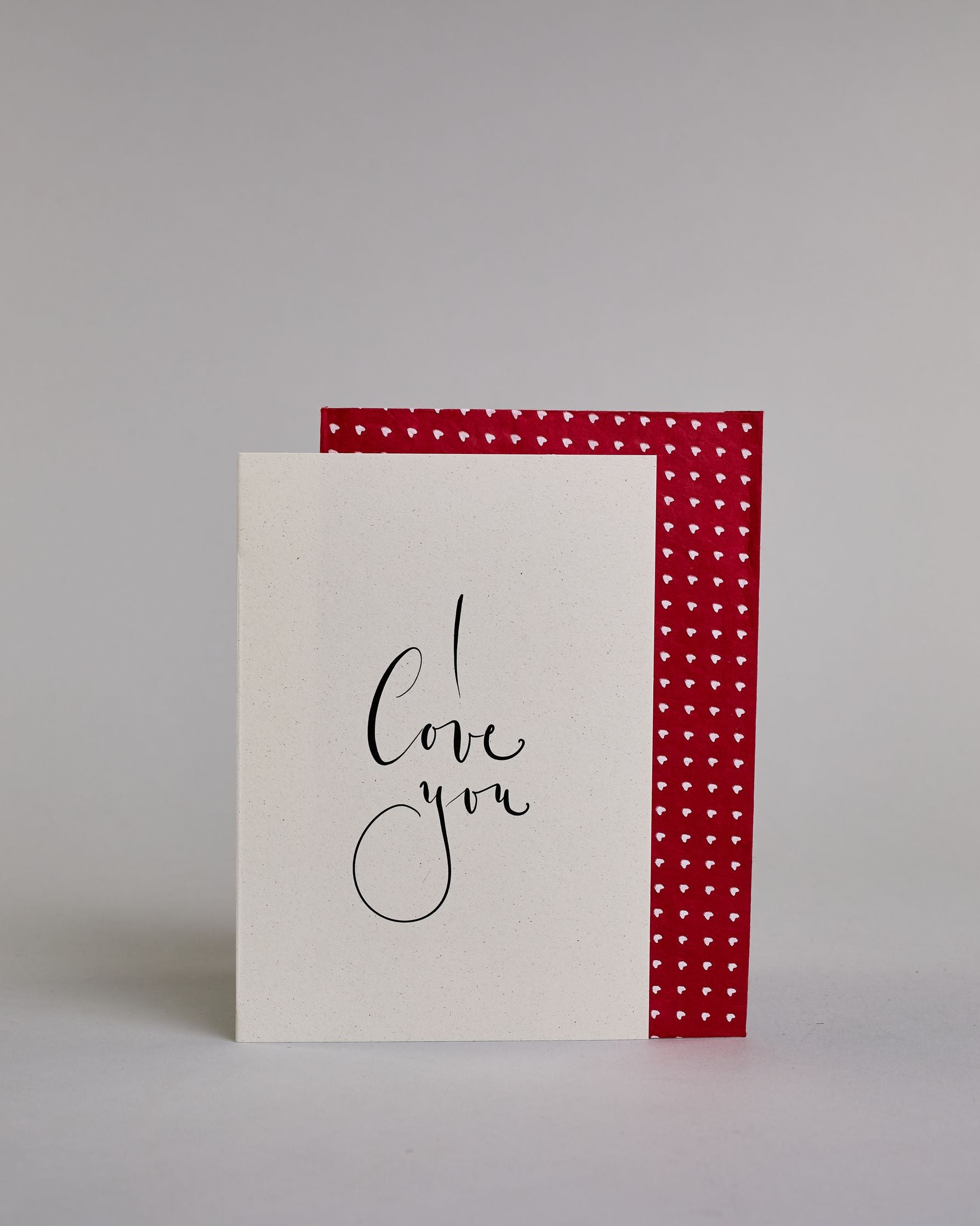 Klappkarte für Liebende in Englisch mit schwarzer Kalligrafieaufschrift "I love you" auf hellem Hintergrund. Der Text ist in drei Zeilen mit jeweils einem Wort aufgeteilt und in einer kunstvollen Schreibschrif gestaltet. Dazu ein grün-goldenes handgeschöpftes Kuvert. #2