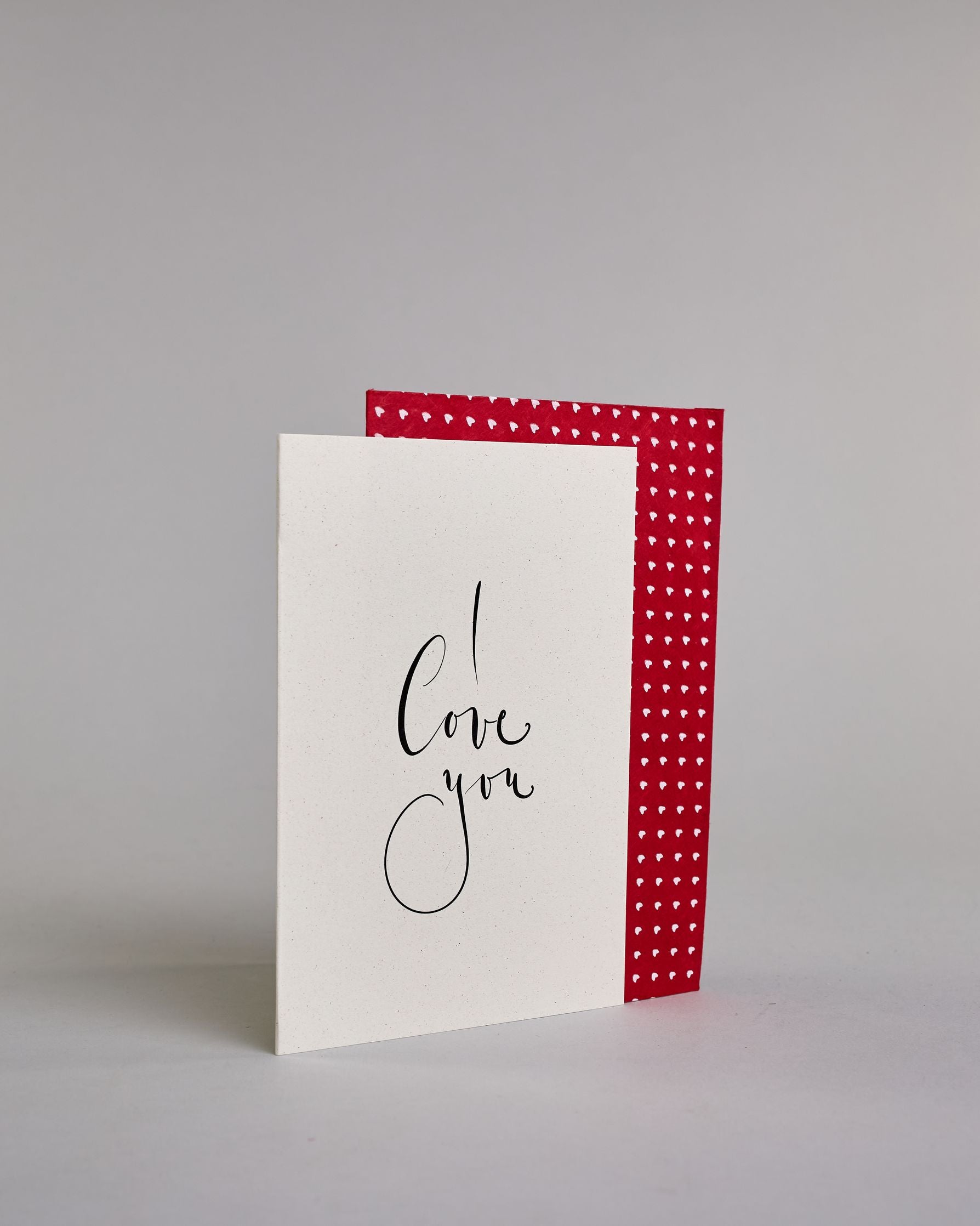 Klappkarte für Liebende in Englisch mit schwarzer Kalligrafieaufschrift "I love you" auf hellem Hintergrund. Der Text ist in drei Zeilen mit jeweils einem Wort aufgeteilt und in einer kunstvollen Schreibschrif gestaltet. Dazu ein grün-goldenes handgeschöpftes Kuvert. #3