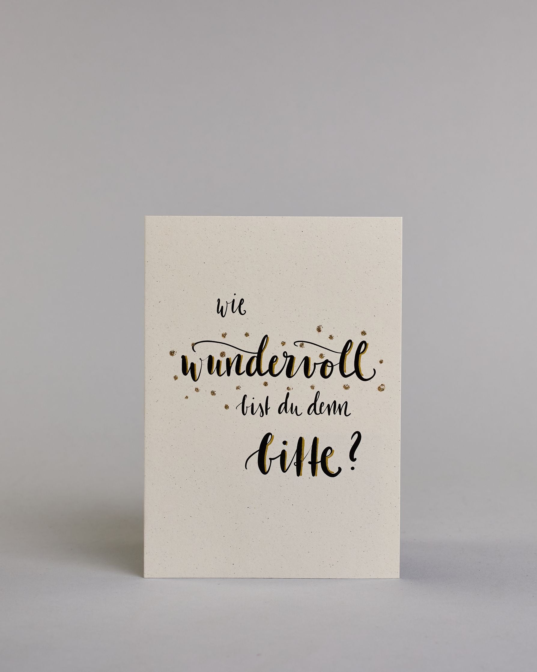 Klappkarte für Liebende mit schwarzer Kalligrafieaufschrift "Wie wundervoll bist du denn bitte?" auf hellem Hintergrund. Der Text ist in folgende vier Zeilen aufgeteilt: "wie" in dünner Schreibschrift, darunter "wundervoll" in verschnörkelter Schreibschrift mit glitzernden Punkten rundherum, darunter "bist du denn" in der gleichen Schrift wie die erste Zeile, darunter "bitte?" in der gleichen Schrift wie die zweite Zeile. Dazu ein gold-weißes handgeschöpftes Kuvert. #1