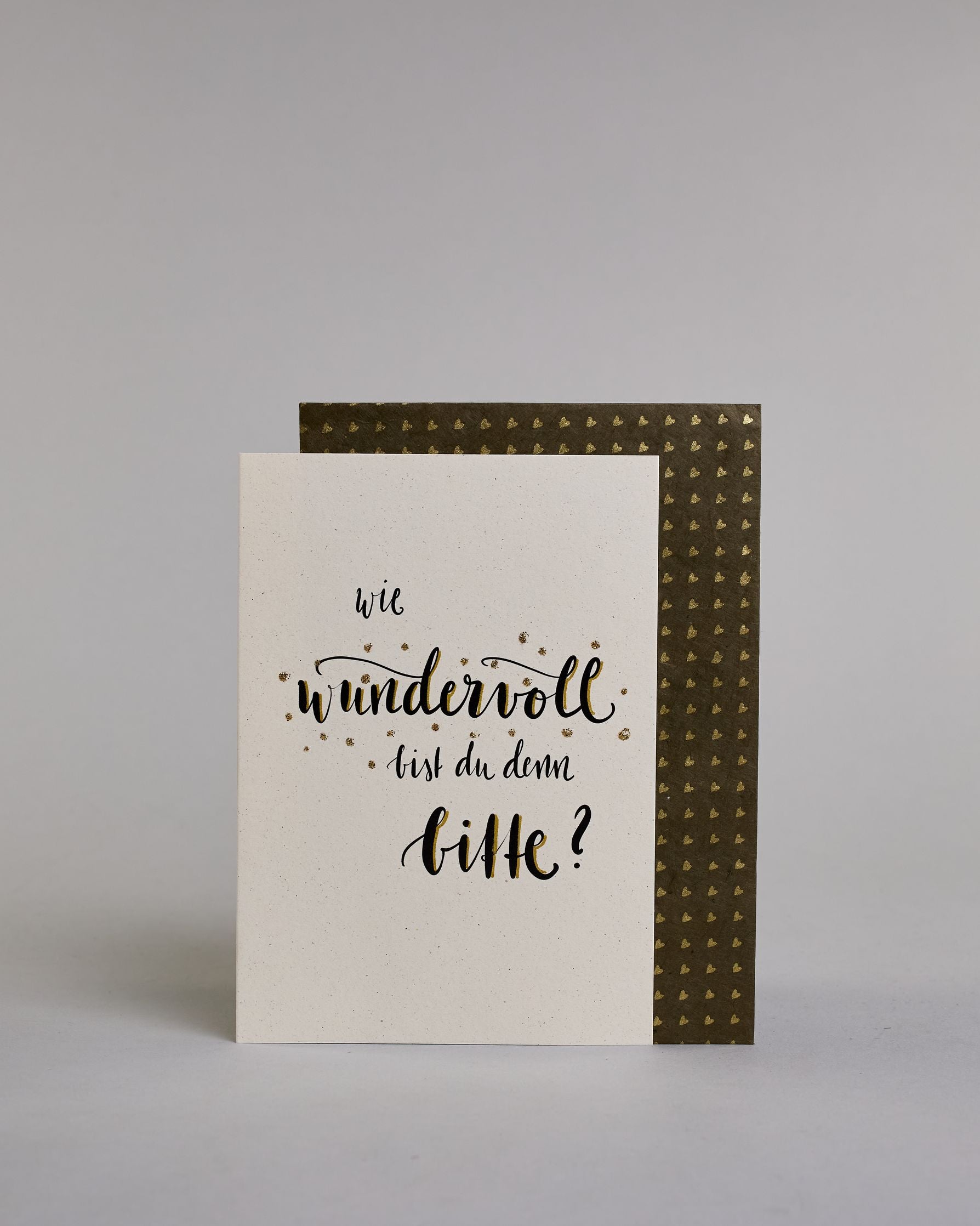Klappkarte für Liebende mit schwarzer Kalligrafieaufschrift "Wie wundervoll bist du denn bitte?" auf hellem Hintergrund. Der Text ist in folgende vier Zeilen aufgeteilt: "wie" in dünner Schreibschrift, darunter "wundervoll" in verschnörkelter Schreibschrift mit glitzernden Punkten rundherum, darunter "bist du denn" in der gleichen Schrift wie die erste Zeile, darunter "bitte?" in der gleichen Schrift wie die zweite Zeile. Dazu ein gold-weißes handgeschöpftes Kuvert. #2