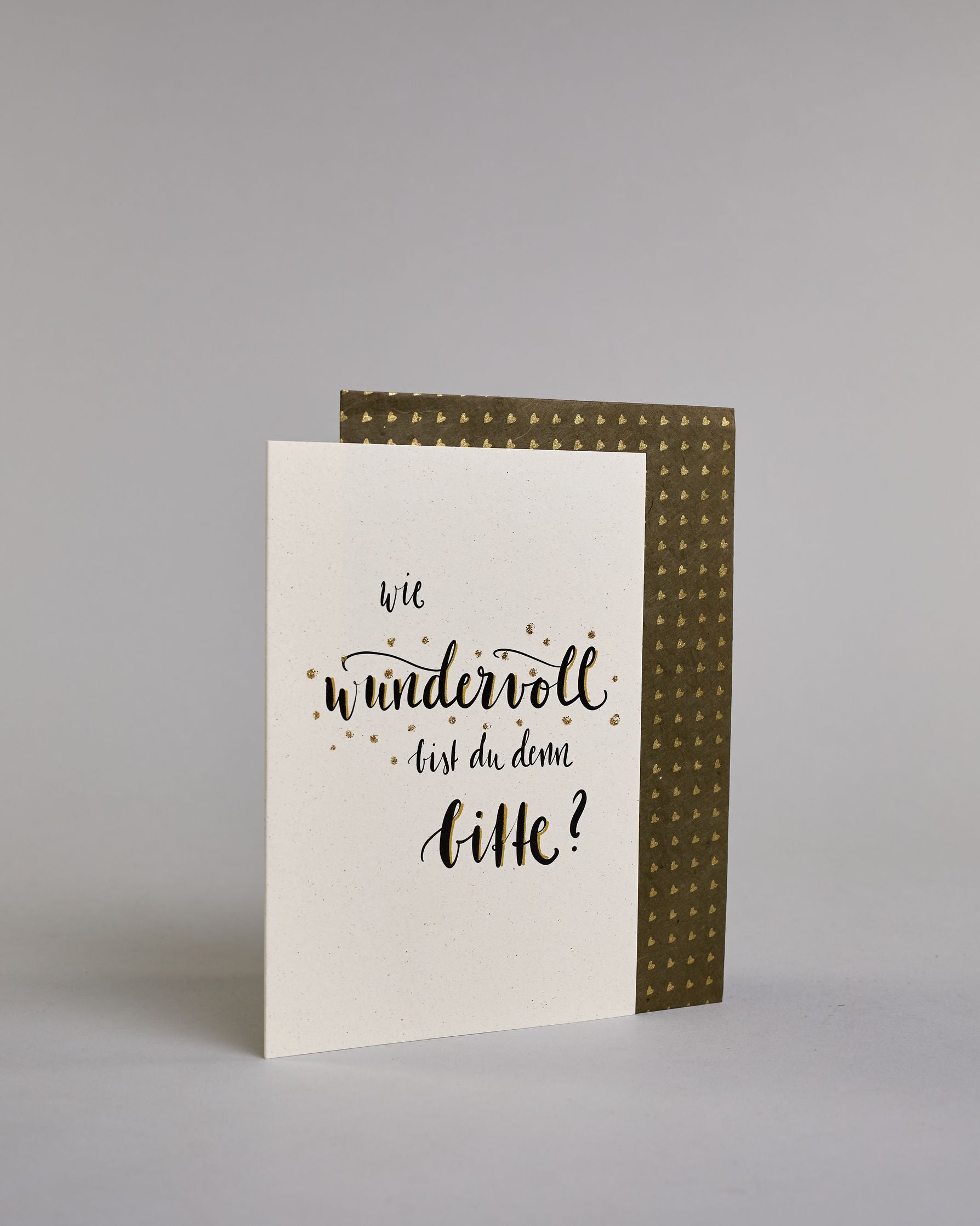 Klappkarte für Liebende mit schwarzer Kalligrafieaufschrift "Wie wundervoll bist du denn bitte?" auf hellem Hintergrund. Der Text ist in folgende vier Zeilen aufgeteilt: "wie" in dünner Schreibschrift, darunter "wundervoll" in verschnörkelter Schreibschrift mit glitzernden Punkten rundherum, darunter "bist du denn" in der gleichen Schrift wie die erste Zeile, darunter "bitte?" in der gleichen Schrift wie die zweite Zeile. Dazu ein gold-weißes handgeschöpftes Kuvert. #3