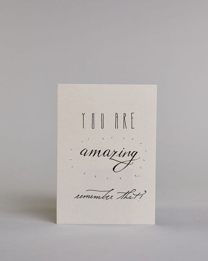 Klappkarte für Liebende auf Englisch mit schwarzer Kalligrafieaufschrift "You are amazing remeber that!" auf hellem Hintergrund. Der Text ist in folgende vier Zeilen aufgeteilt: "YOU ARE" in dünner gerader Kalligrafieschrift, darunter "amazing" in großer Schreibschrift und einem Konfettiähnlichen Kranz um das Wort herum, darunter "remember that!", in dünner kleiner Schreibschrift. Dazu ein handgeschöpftes Kuvert. #1